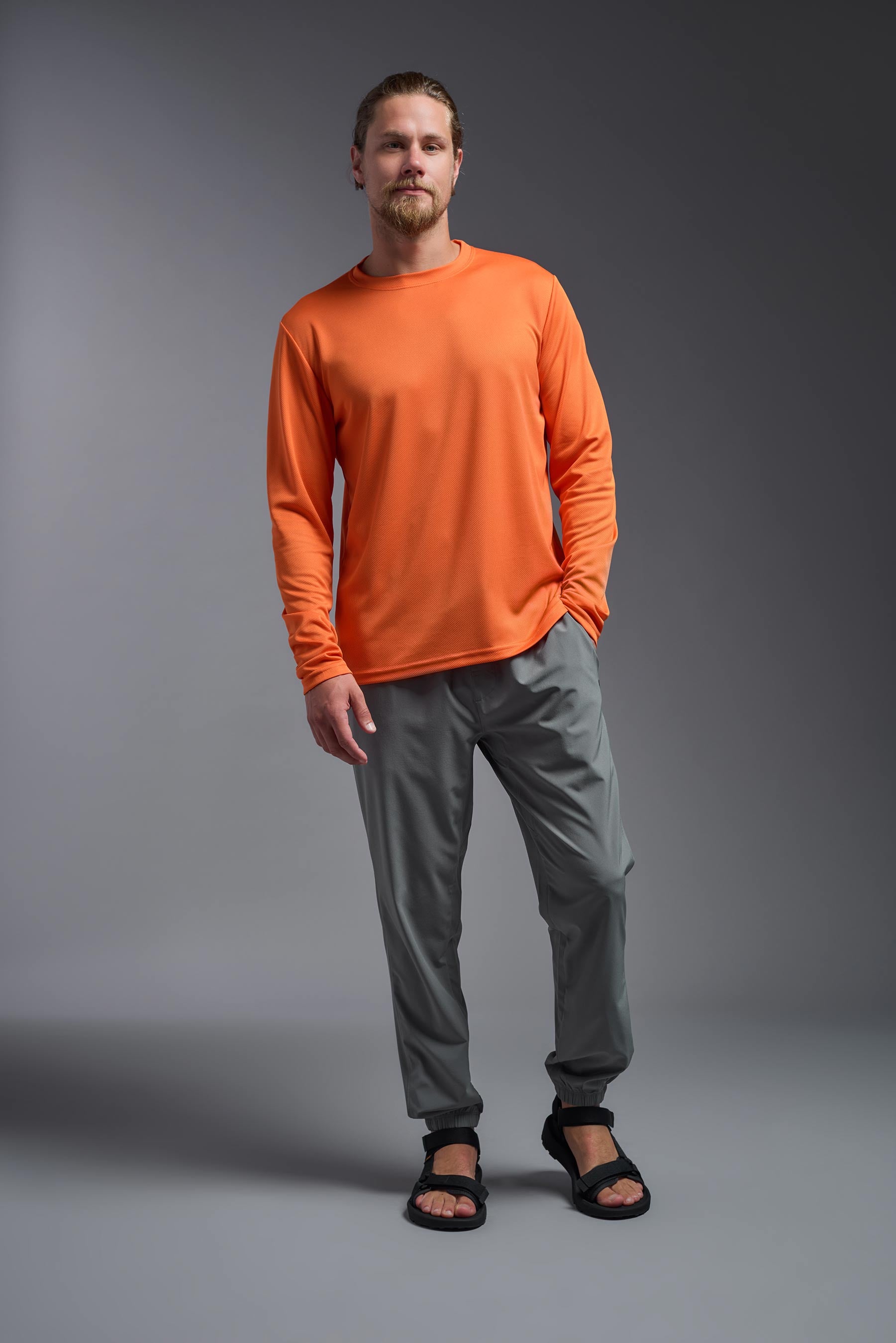 A male model wearing the men's Oxymesh Long Sleeve Tech Tee in the color orange, made out of 100% polyester, showing the relaxed fit from a front view. This shirt is breathable, quick-drying, moisture-wicking, and made in the USA. #orange