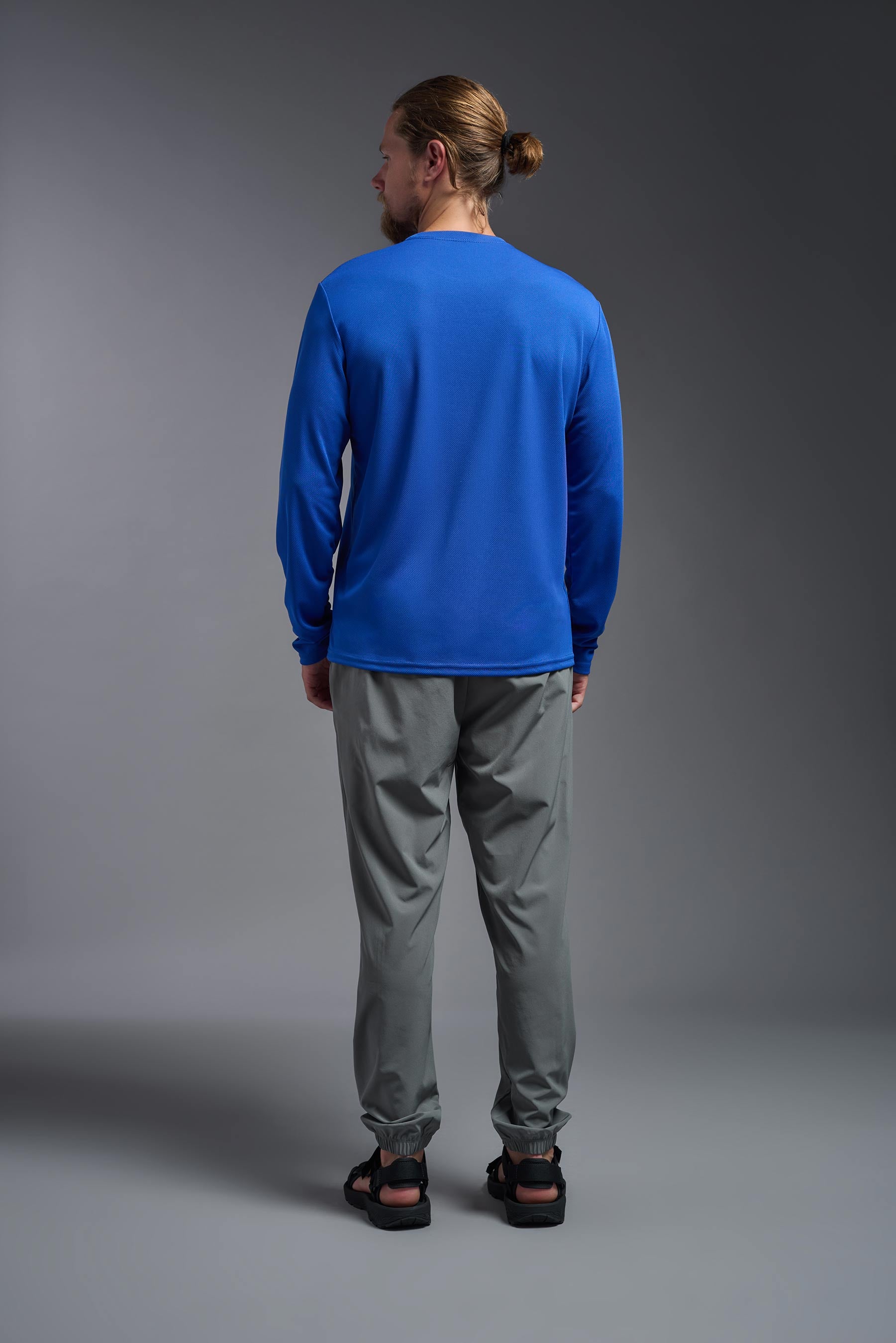 A male model wearing the men's Oxymesh Long Sleeve Tech Tee in the color royal blue, made out of 100% polyester, showing the relaxed fit from a back view. This shirt is breathable, quick-drying, moisture-wicking, and made in the USA. #royal-blue