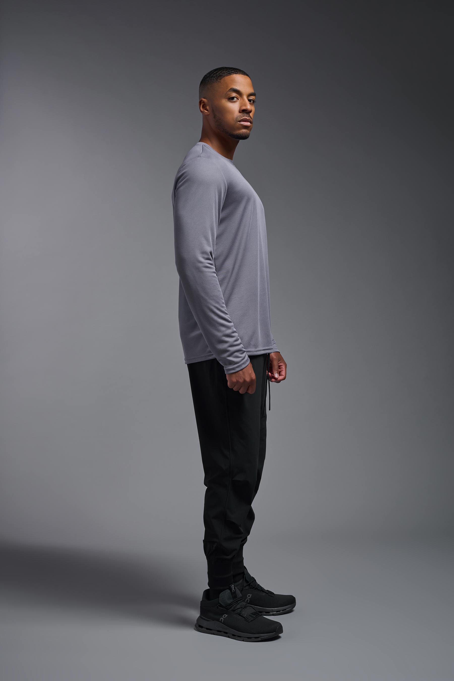 A male model wearing the men's Oxymesh Long Sleeve Tech Tee in the color steel gray made out of 100% polyester, showing the relaxed fit from a side view. This shirt is breathable, quick-drying, moisture-wicking, and made in the USA. #steel-gray