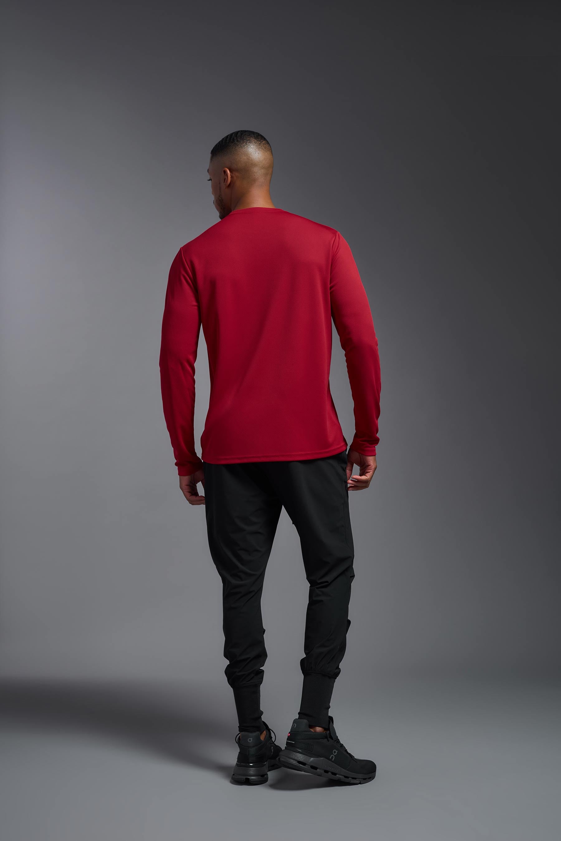 A male model wearing the men's Oxymesh Long Sleeve Tech Tee in the color true red made out of 100% polyester, showing the relaxed fit from a back view. This shirt is breathable, quick-drying, moisture-wicking, and made in the USA. #true-red