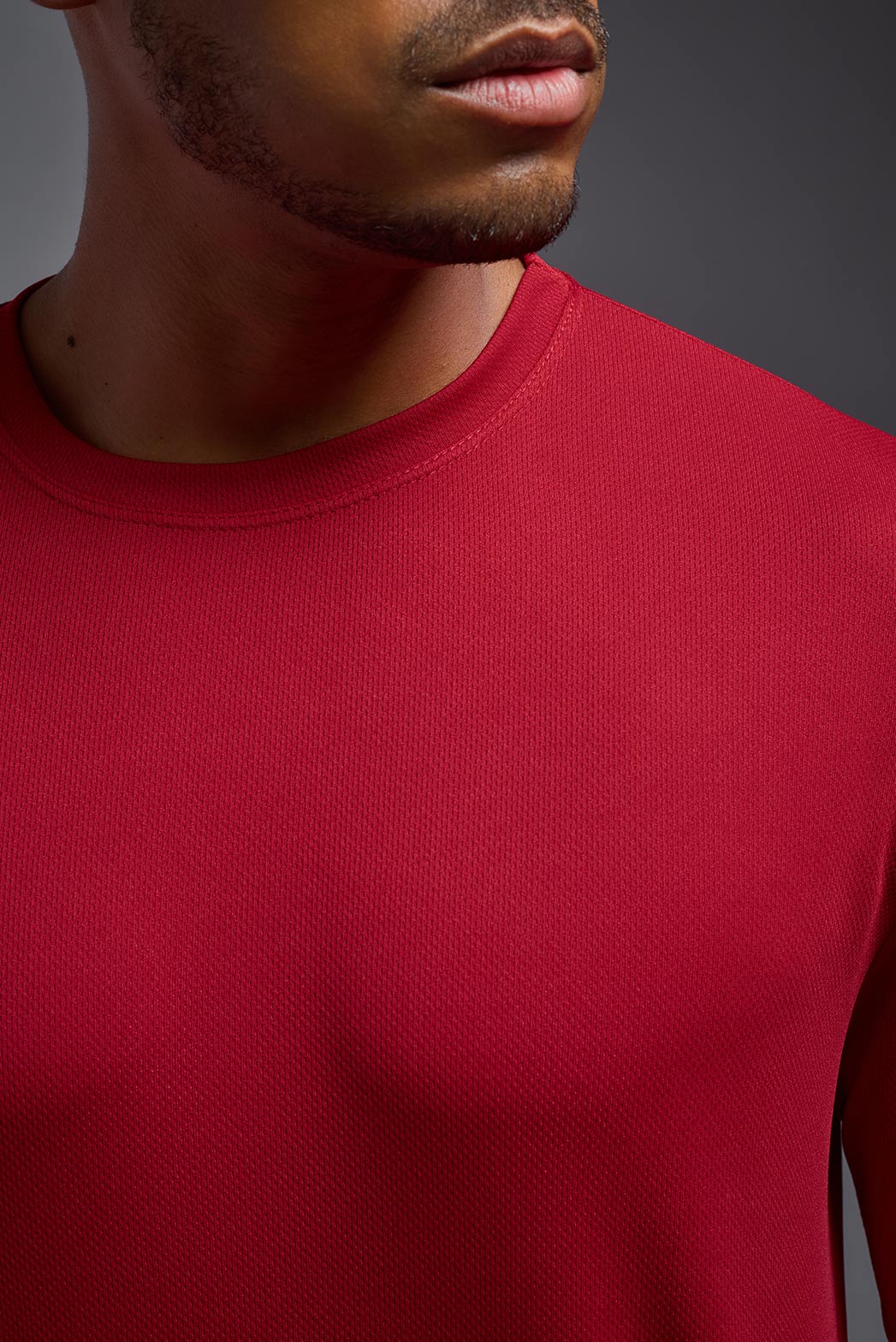 A male model wearing the men's Oxymesh Long Sleeve Tech Tee in the color true red made out of 100% polyester, showing the relaxed fit from a close-up collar view. This shirt is breathable, quick-drying, moisture-wicking, and made in the USA. #true-red