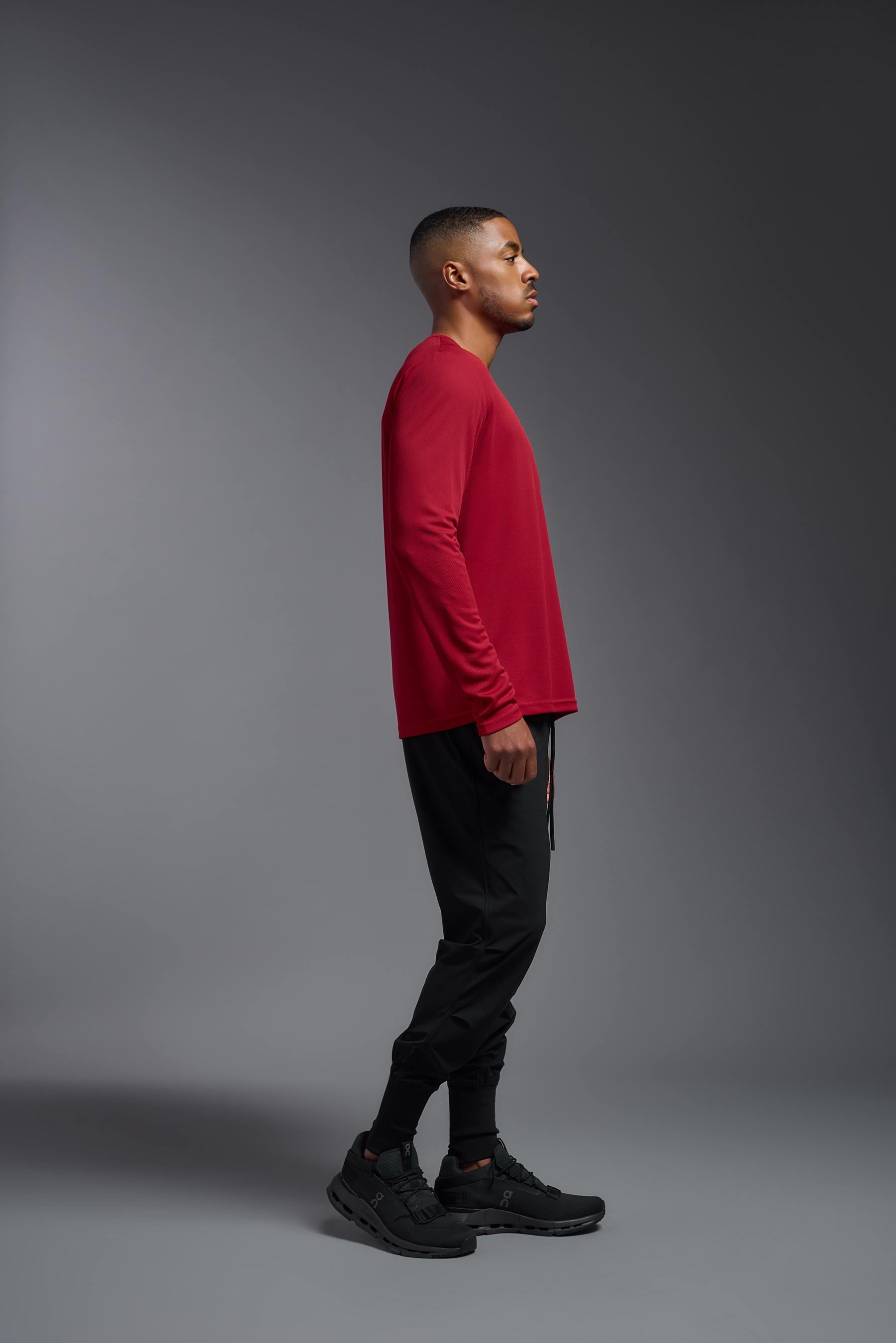 A male model wearing the men's Oxymesh Long Sleeve Tech Tee in the color true red made out of 100% polyester, showing the relaxed fit from a side view. This shirt is breathable, quick-drying, moisture-wicking, and made in the USA. #true-red