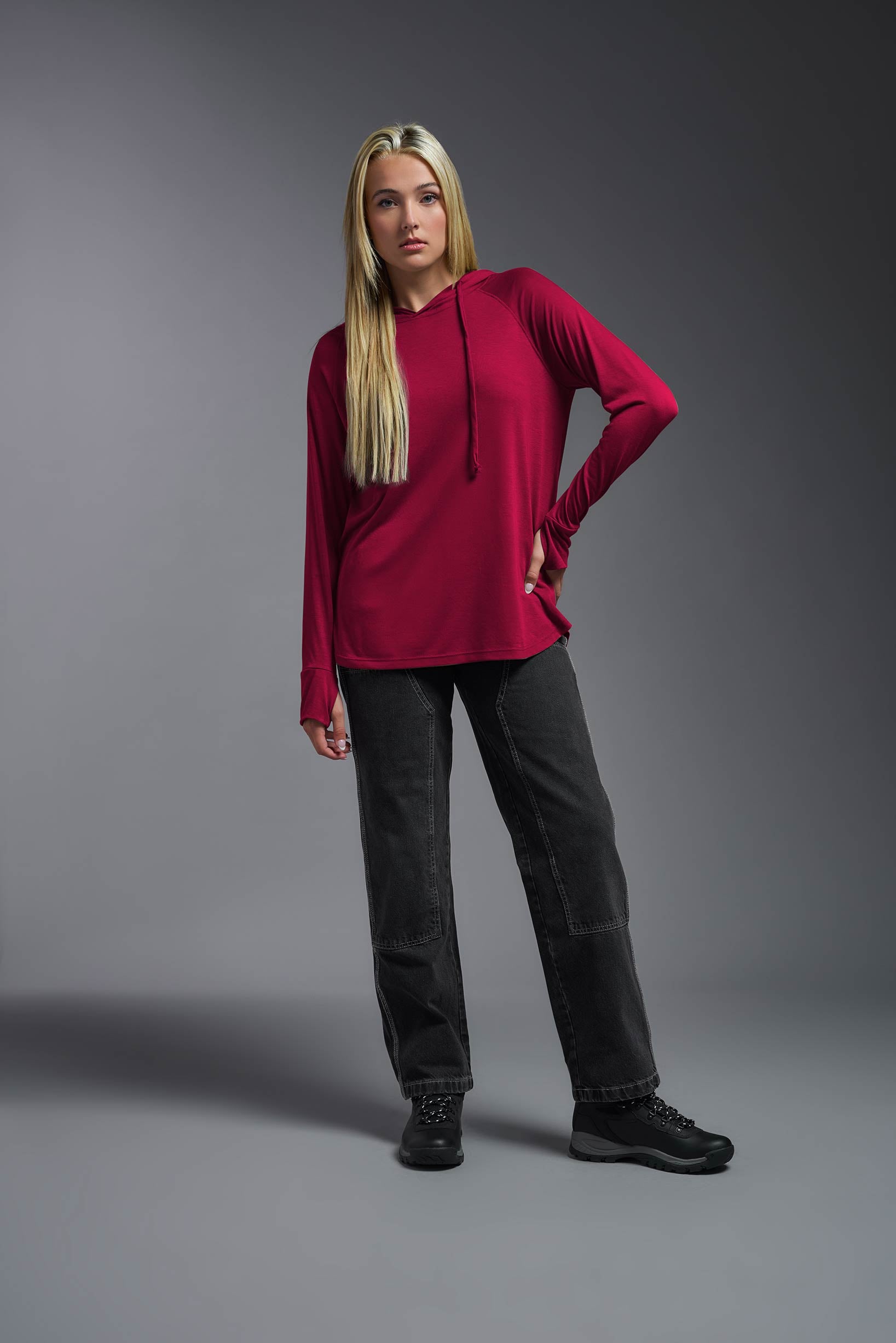 A female model wearing the women's Siro™ Curvy Hoodie Shirt in the color scarlet, made out of 100% filament polyester, showing the relaxed fit from a front view. This long sleeve hoodie shirt is breathable, quick-drying, moisture-wicking, and made in the USA. #scarlet