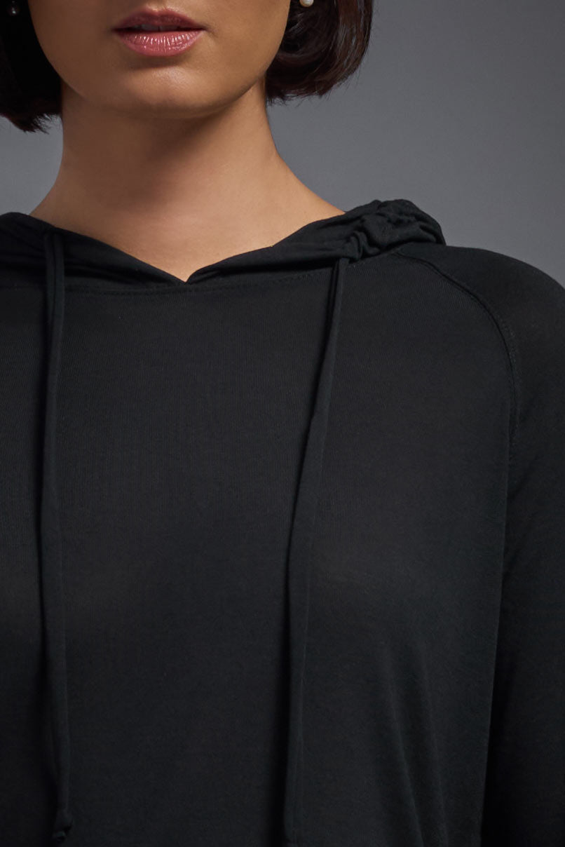 A female model wearing the women's Siro™ Hoodie Shirt in the color black, made out of 100% filament polyester, showing the relaxed fit from a front closeup collar view. This long sleeve hoodie shirt is breathable, quick-drying, moisture-wicking, and made in the USA. #black