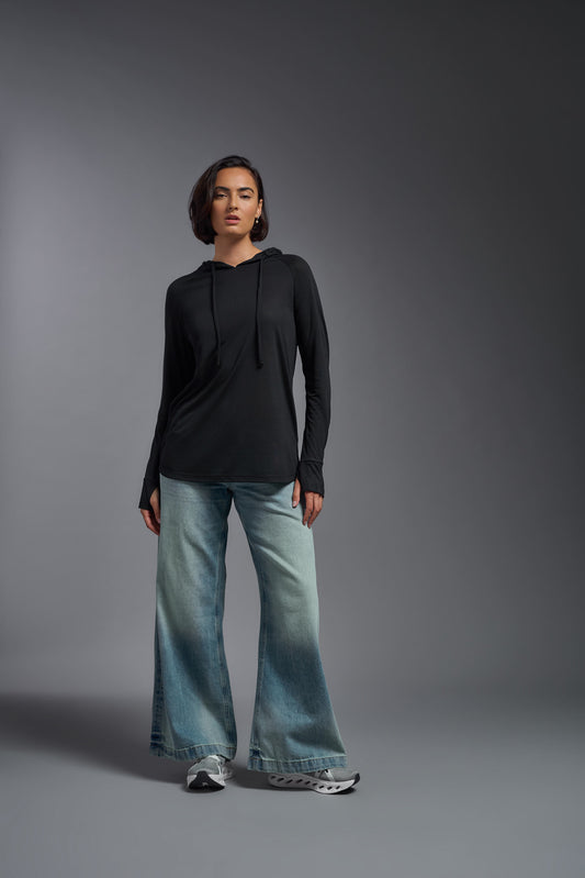 A female model wearing the women's Siro™ Hoodie Shirt in the color black, made out of 100% filament polyester, showing the relaxed fit from a front view. This long sleeve hoodie shirt is breathable, quick-drying, moisture-wicking, and made in the USA. #black