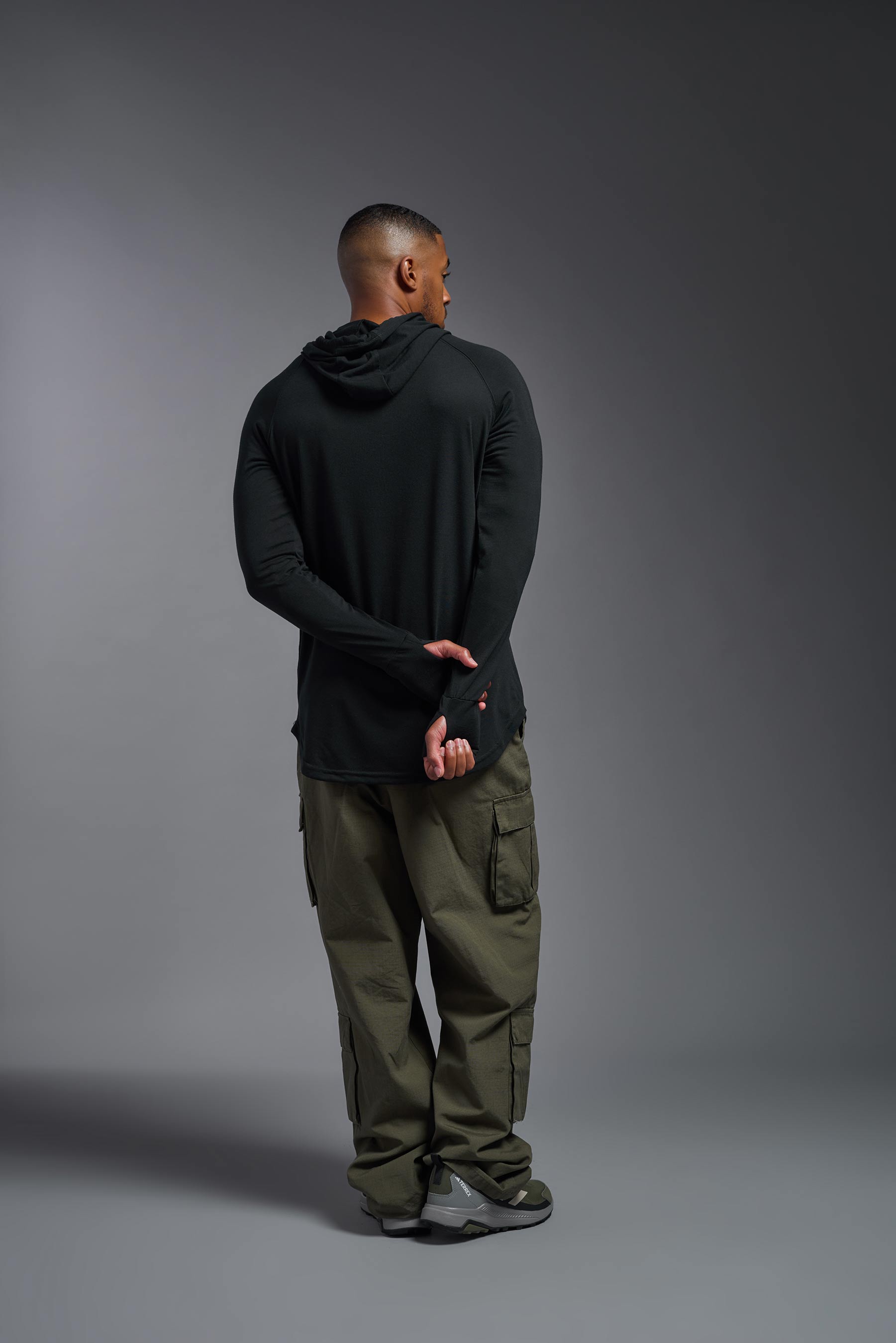 A male model wearing the men's Siro™ Hoodie Shirt in the color black, made out of 100% polyester, showing the relaxed fit from a back view. This long sleeve hoodie shirt is breathable, quick-drying, moisture-wicking, and made in the USA. #black