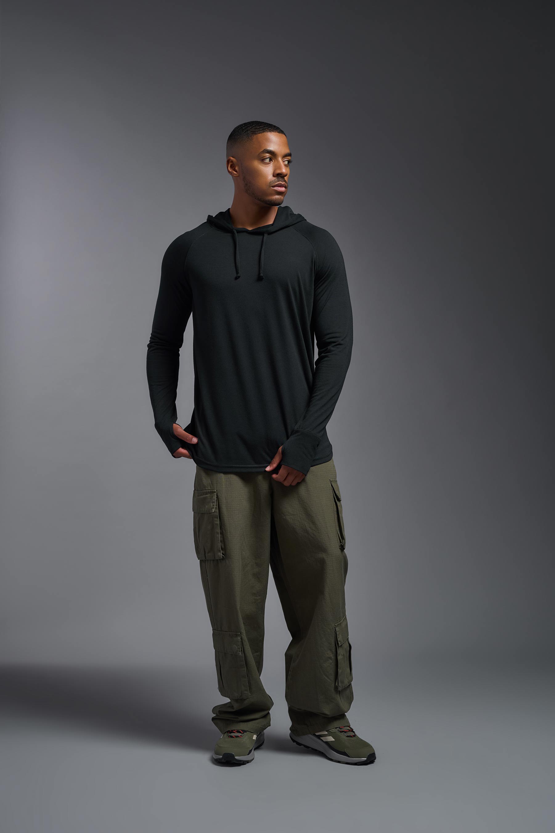 A male model wearing the men's Siro™ Hoodie Shirt in the color black, made out of 100% polyester, showing the relaxed fit from a front view. This long sleeve hoodie shirt is breathable, quick-drying, moisture-wicking, and made in the USA. #black