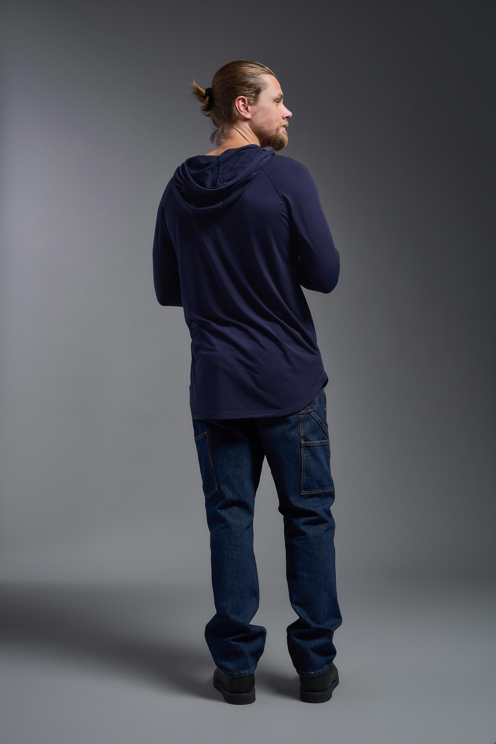 A male model wearing the men's Siro™ Hoodie Shirt in the color navy, made out of 100% polyester, showing the relaxed fit from a back view. This long sleeve hoodie shirt is breathable, quick-drying, moisture-wicking, and made in the USA. #navy