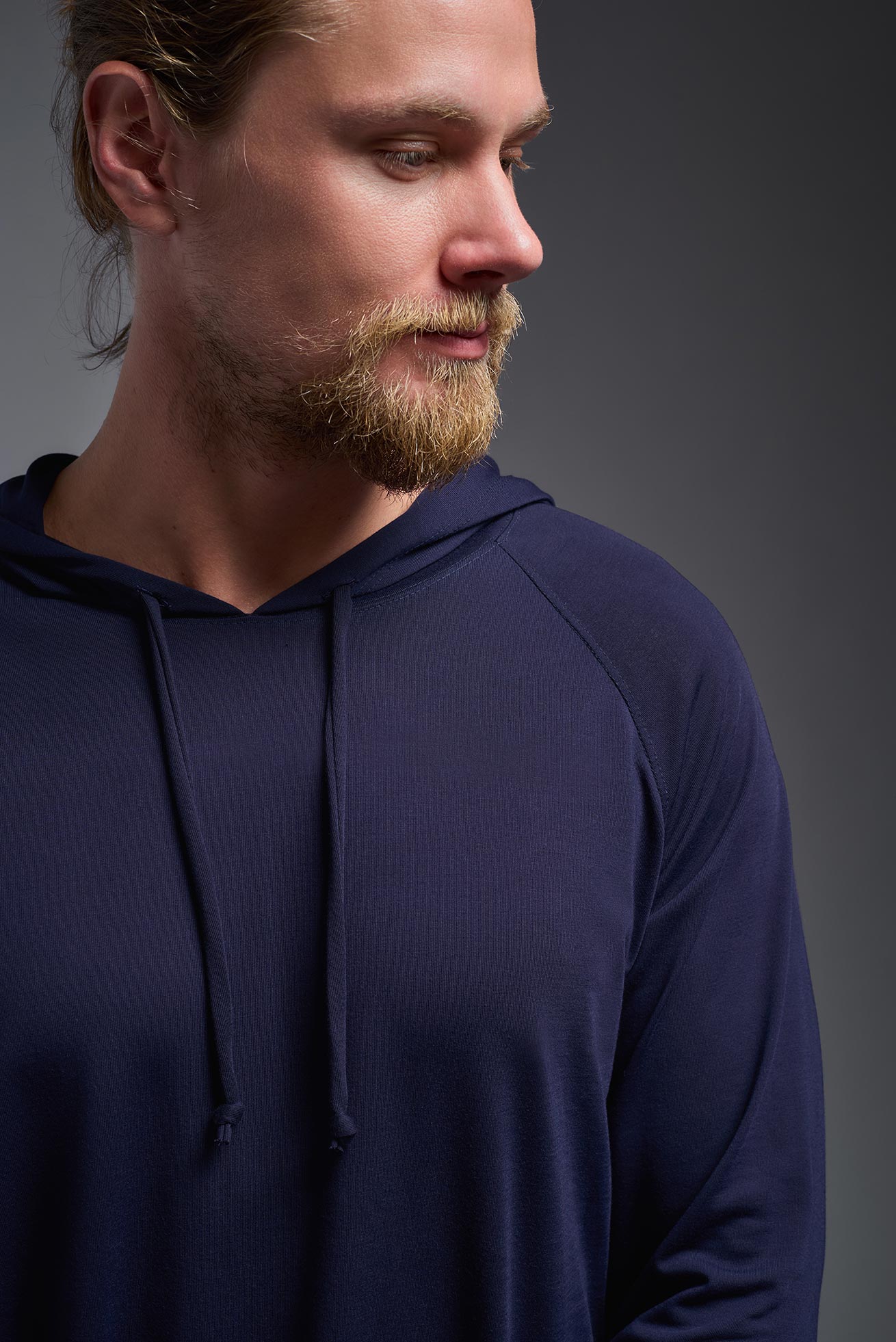 A male model wearing the men's Siro™ Hoodie Shirt in the color navy, made out of 100% polyester, showing the relaxed fit from a closeup front collar view. This long sleeve hoodie shirt is breathable, quick-drying, moisture-wicking, and made in the USA. #navy