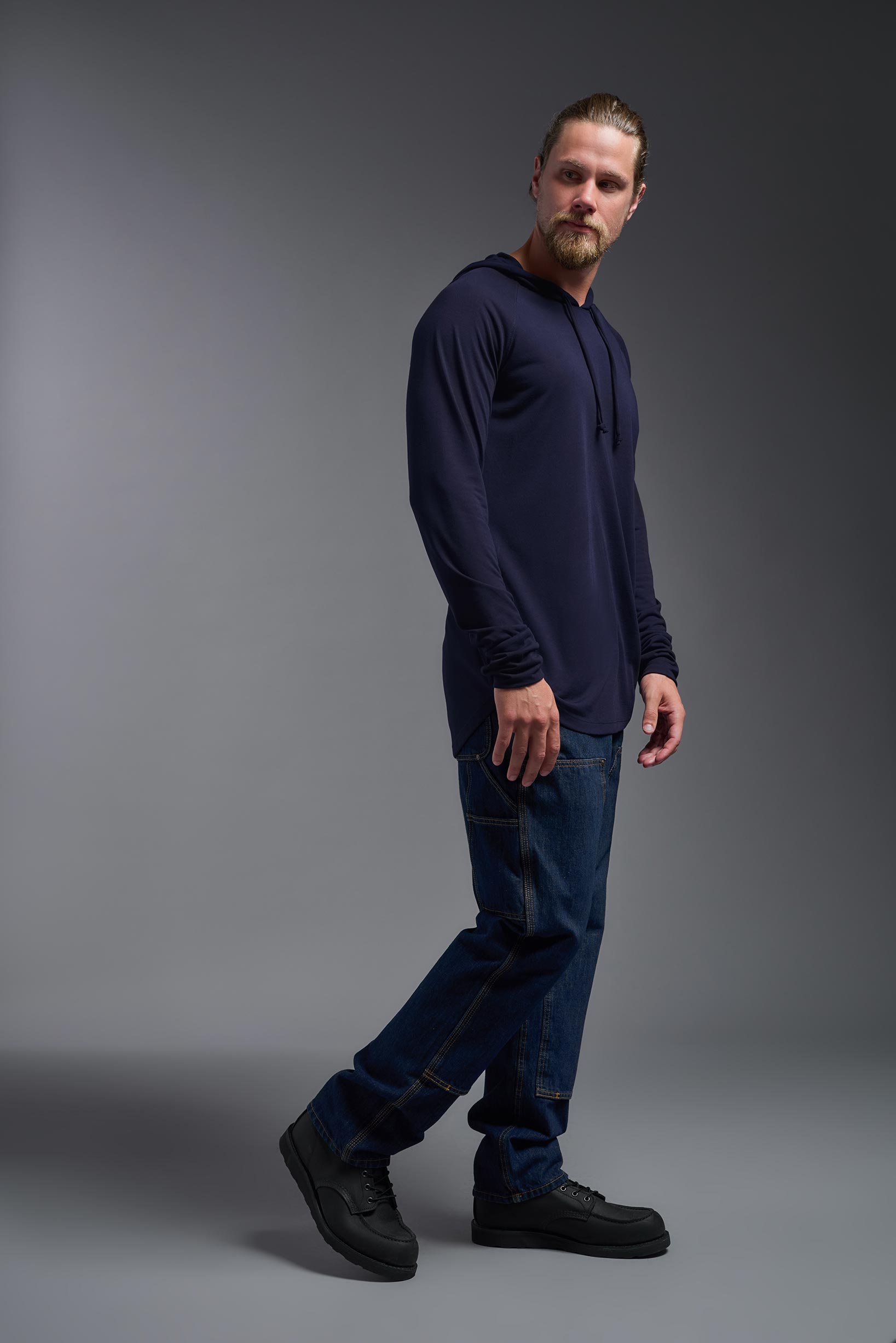 A male model wearing the men's Siro™ Hoodie Shirt in the color navy, made out of 100% polyester, showing the relaxed fit from a side view. This long sleeve hoodie shirt is breathable, quick-drying, moisture-wicking, and made in the USA. #navy