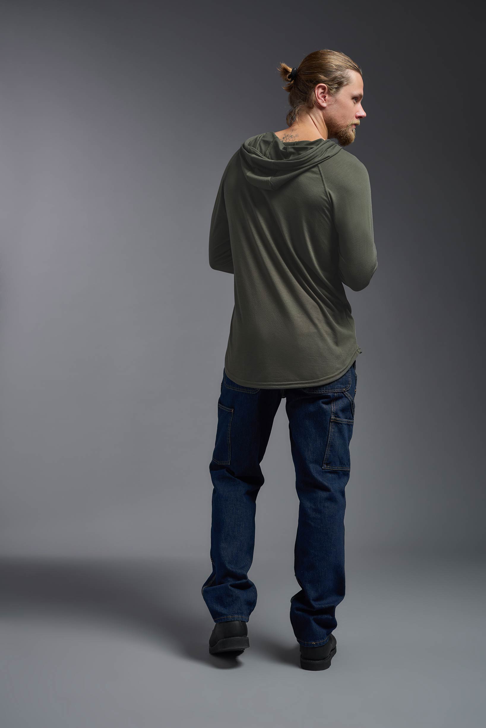 A male model wearing the men's Siro™ Hoodie Shirt in the color olive, made out of 100% polyester, showing the relaxed fit from a back view. This long sleeve hoodie shirt is breathable, quick-drying, moisture-wicking, and made in the USA. #olive