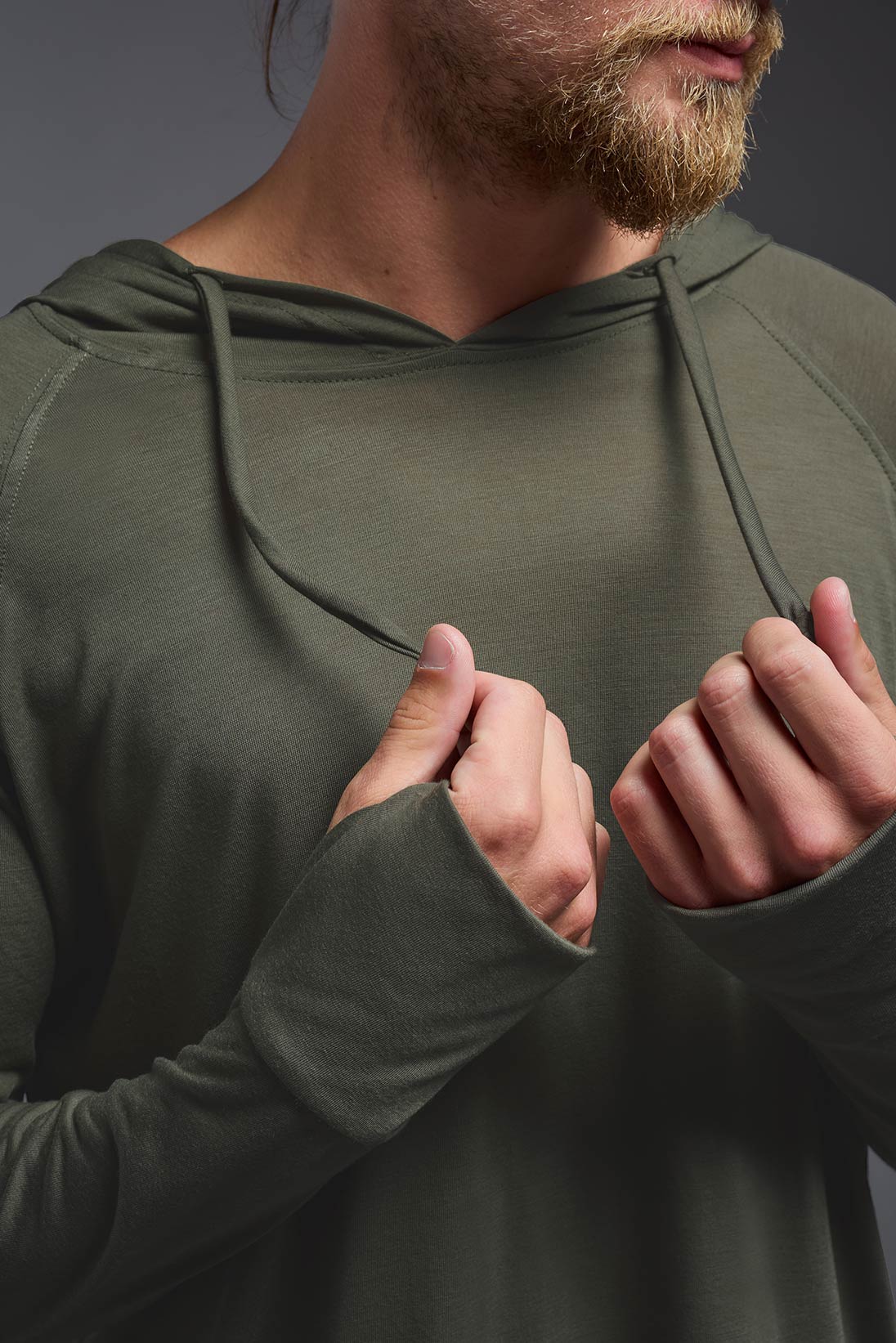 A male model wearing the men's Siro™ Hoodie Shirt in the color olive, made out of 100% polyester, showing the relaxed fit from a closeup collar front view. This long sleeve hoodie shirt is breathable, quick-drying, moisture-wicking, and made in the USA. #olive