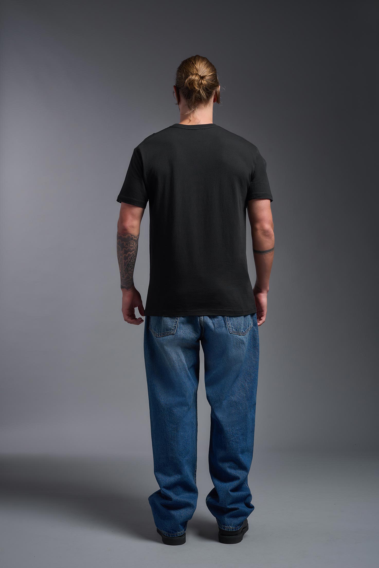 A male model wearing the unisex Americana Cotton Soft Tee in the color black, made from 100% combed ring-spun USA-grown cotton, showing the classic fit from a back view. This premium shirt is Made in the USA. #black