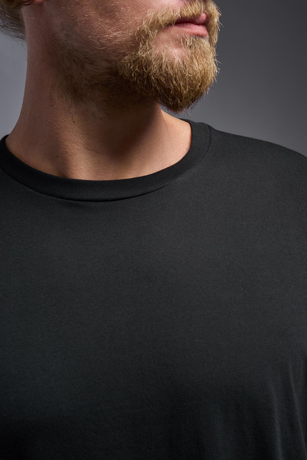 A male model wearing the unisex Americana Cotton Soft Tee in the color black, made from 100% combed ring-spun USA-grown cotton, showing the classic fit from a close-up collar view. This premium shirt is Made in the USA. #black