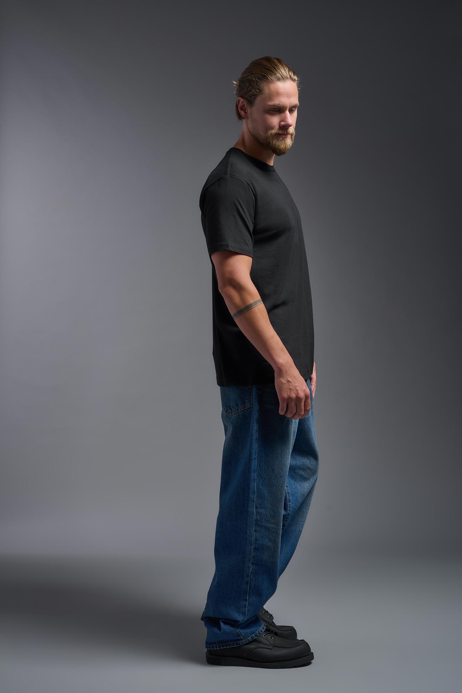 A male model wearing the unisex Americana Cotton Soft Tee in the color black, made from 100% combed ring-spun USA-grown cotton, showing the classic fit from a side view. This premium shirt is Made in the USA. #black