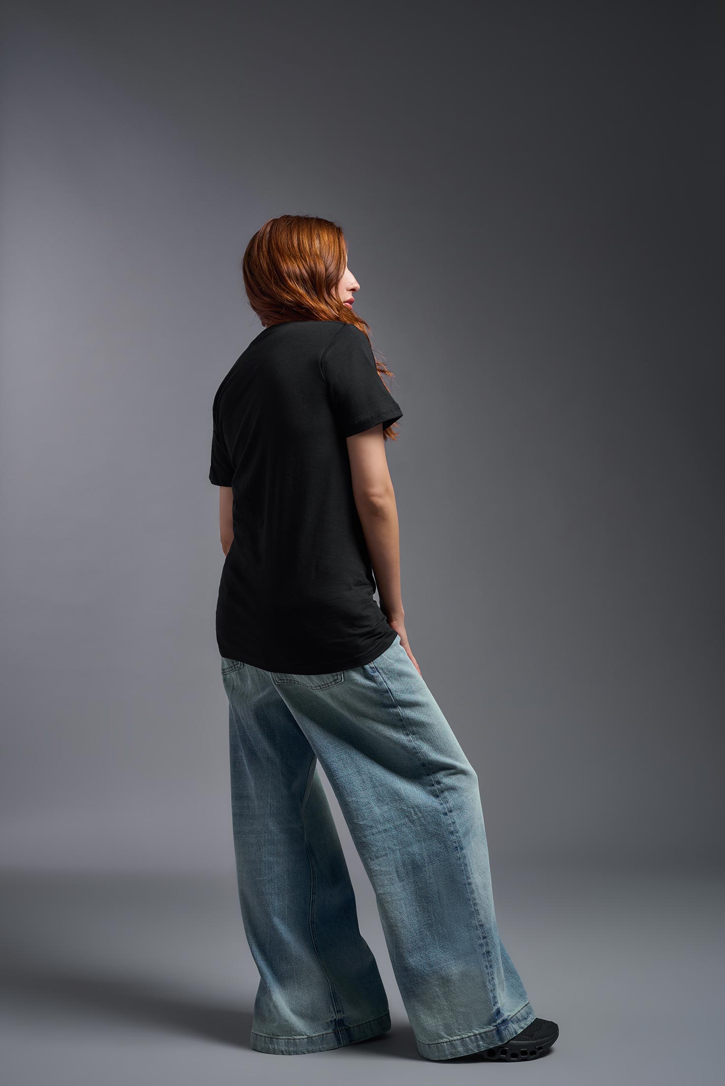A female model wearing the unisex Americana Cotton Soft Tee in the color black, made from 100% combed ring-spun USA-grown cotton, showing the classic fit from a back view. This premium shirt is Made in the USA. #black
