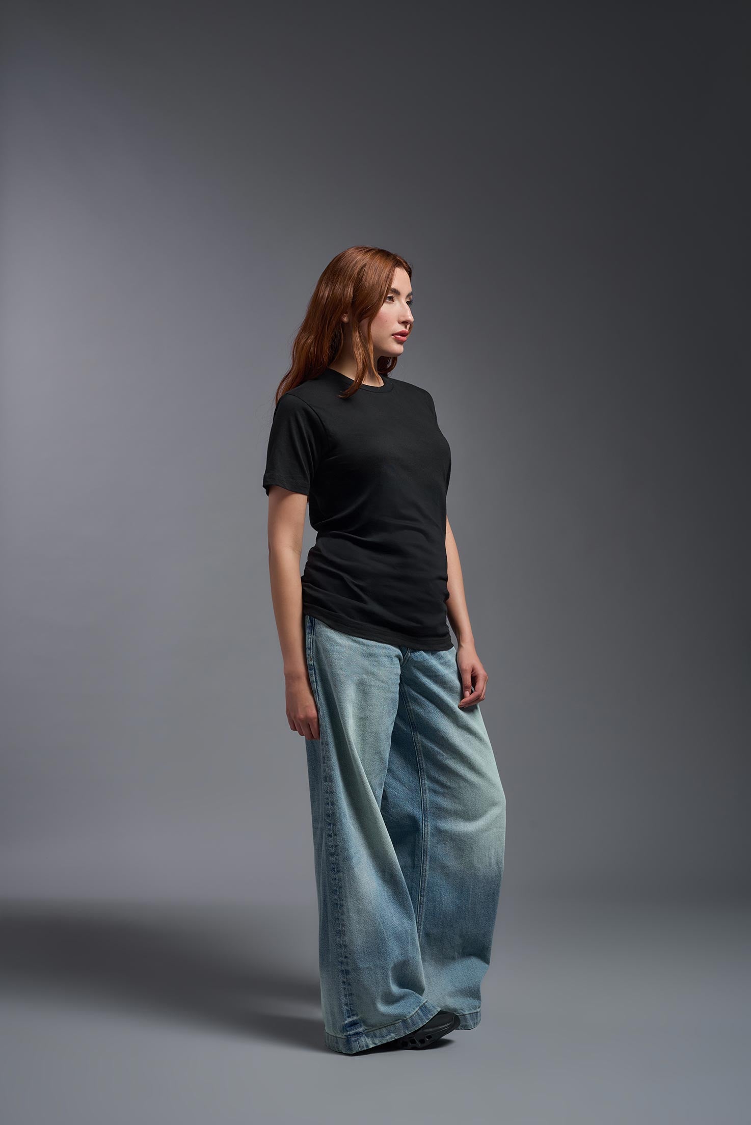 A female model wearing the unisex Americana Cotton Soft Tee in the color black, made from 100% combed ring-spun USA-grown cotton, showing the classic fit from a side view. This premium shirt is Made in the USA. #black