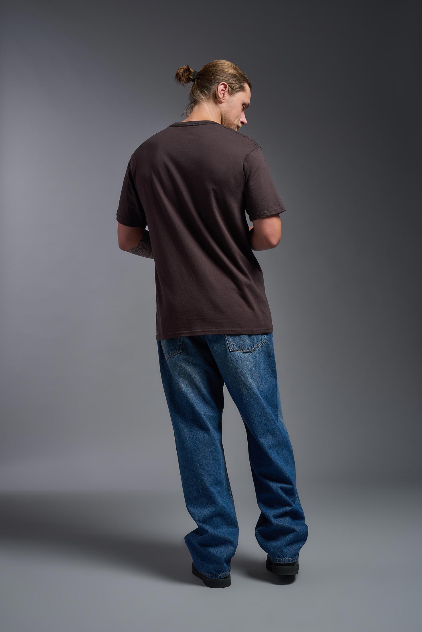 A male model wearing the unisex Americana Cotton Soft Tee in the color brown, made from 100% combed ring-spun USA-grown cotton, showing the classic fit from a back view. This premium shirt is Made in the USA. #brown