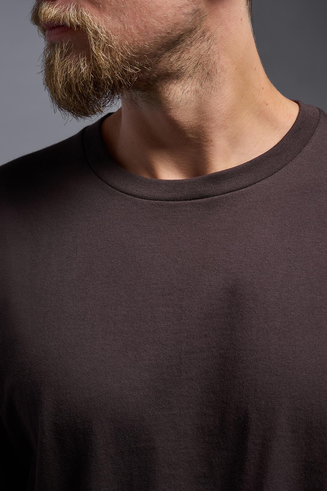 A male model wearing the unisex Americana Cotton Soft Tee in the color brown, made from 100% combed ring-spun USA-grown cotton, showing the classic fit from a close-up collar view. This premium shirt is Made in the USA. #brown