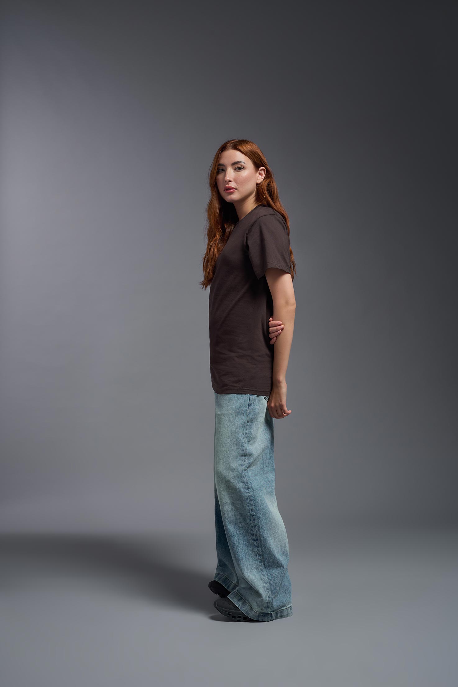 A female model wearing the unisex Americana Cotton Soft Tee in the color brown, made from 100% combed ring-spun USA-grown cotton, showing the classic fit from a side view. This premium shirt is Made in the USA. #brown
