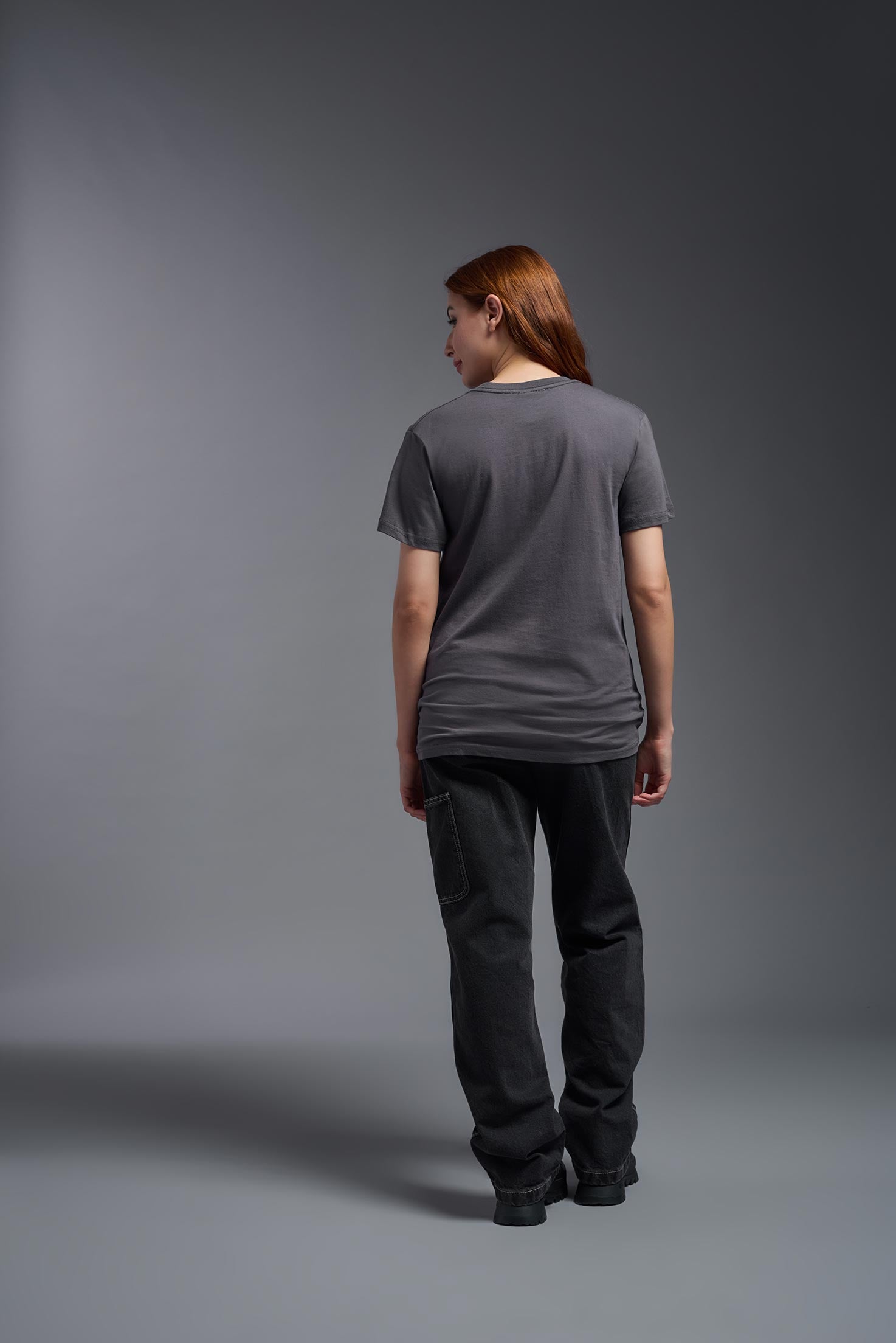 A female model wearing the unisex Americana Cotton Soft Tee in the color charcoal, made from 100% combed ring-spun USA-grown cotton, showing the classic fit from a back view. This premium shirt is Made in the USA. #charcoal