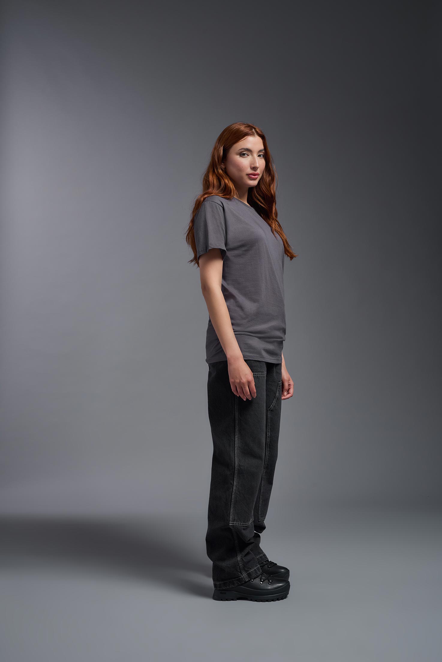 A female model wearing the unisex Americana Cotton Soft Tee in the color charcoal, made from 100% combed ring-spun USA-grown cotton, showing the classic fit from a side view. This premium shirt is Made in the USA. #charcoal