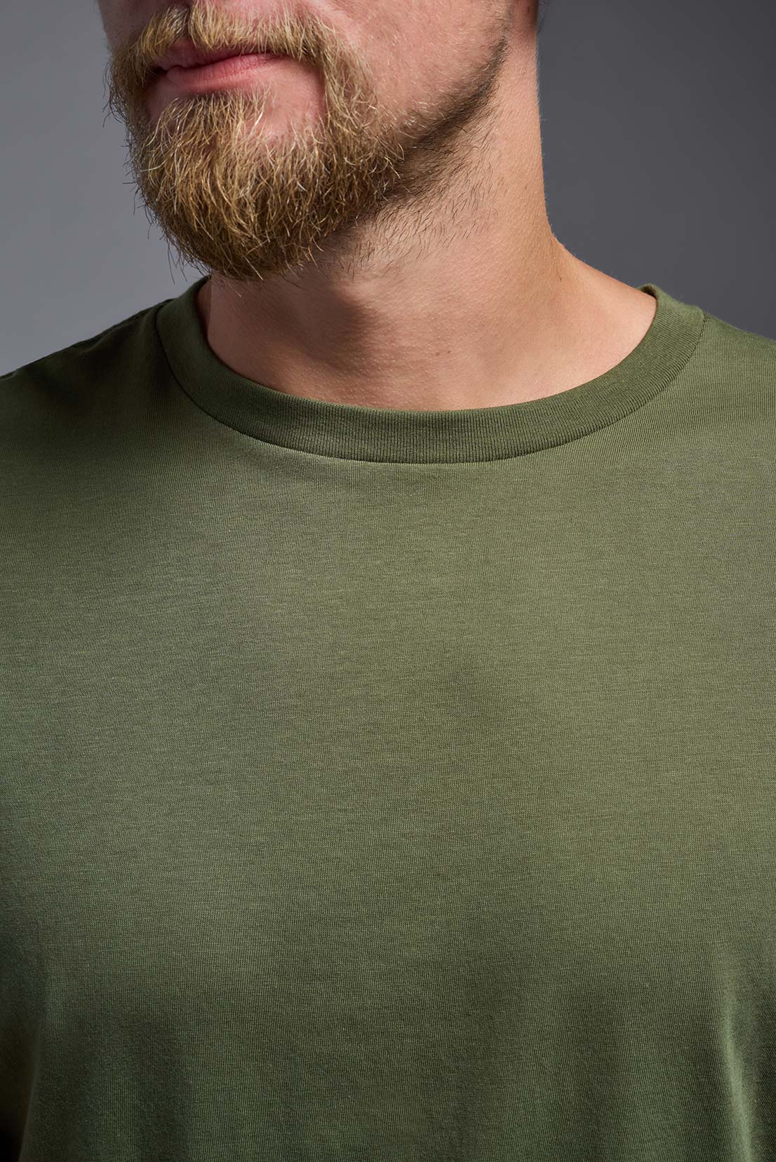A male model wearing the unisex Americana Cotton Soft Tee in the color military green, made from 100% combed ring-spun USA-grown cotton, showing the classic fit from a close-up collar view. This premium shirt is Made in the USA. #military-green