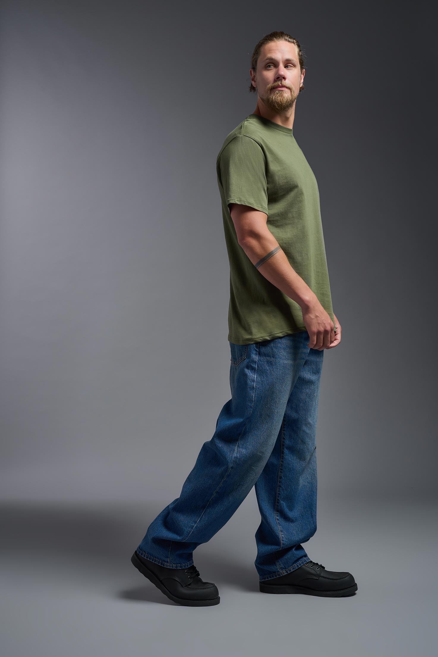A male model wearing the unisex Americana Cotton Soft Tee in the color military green, made from 100% combed ring-spun USA-grown cotton, showing the classic fit from a side view. This premium shirt is Made in the USA. #military-green