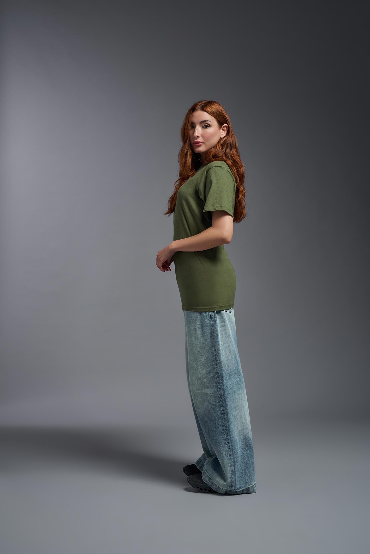 A female model wearing the unisex Americana Cotton Soft Tee in the color military green, made from 100% combed ring-spun USA-grown cotton, showing the classic fit from a side view. This premium shirt is Made in the USA. #military-green