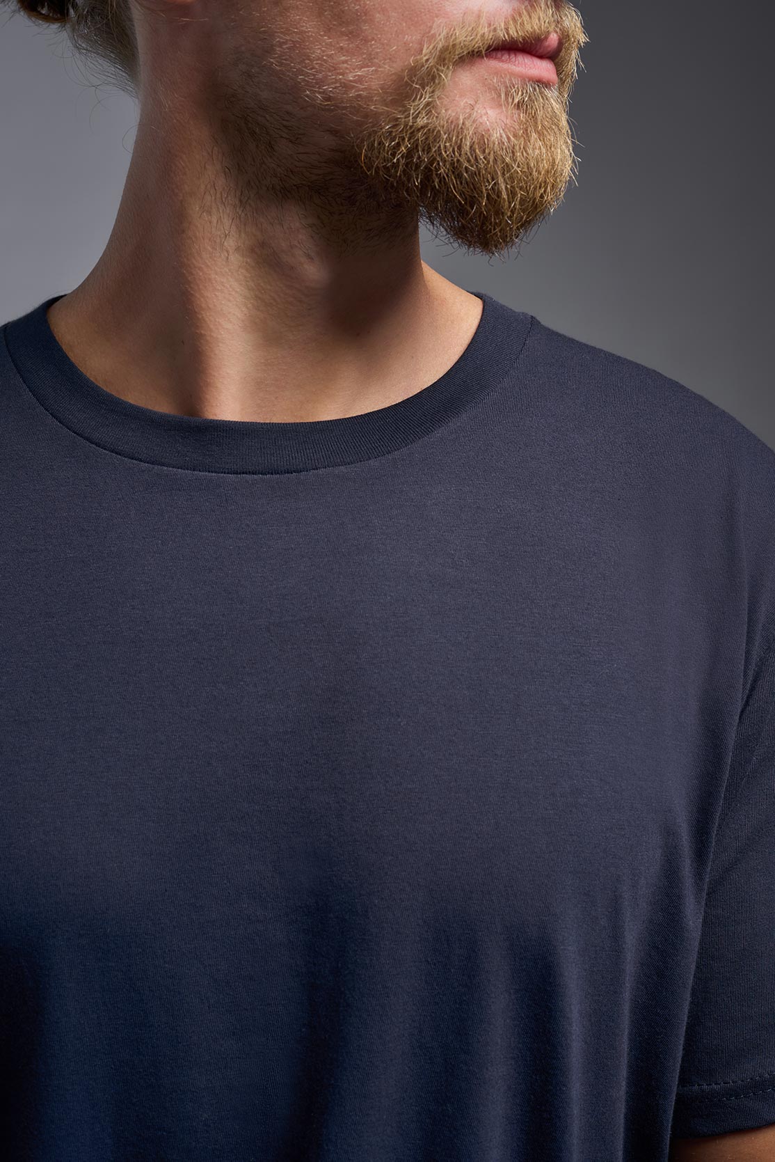 A male model wearing the unisex Americana Cotton Soft Tee in the color navy, made from 100% combed ring-spun USA-grown cotton, showing the classic fit from a close-up collar view. This premium shirt is Made in the USA. #navy