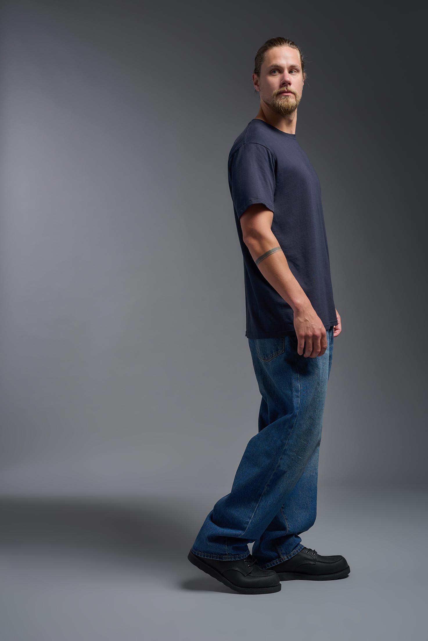 A male model wearing the unisex Americana Cotton Soft Tee in the color navy, made from 100% combed ring-spun USA-grown cotton, showing the classic fit from a side view. This premium shirt is Made in the USA. #navy