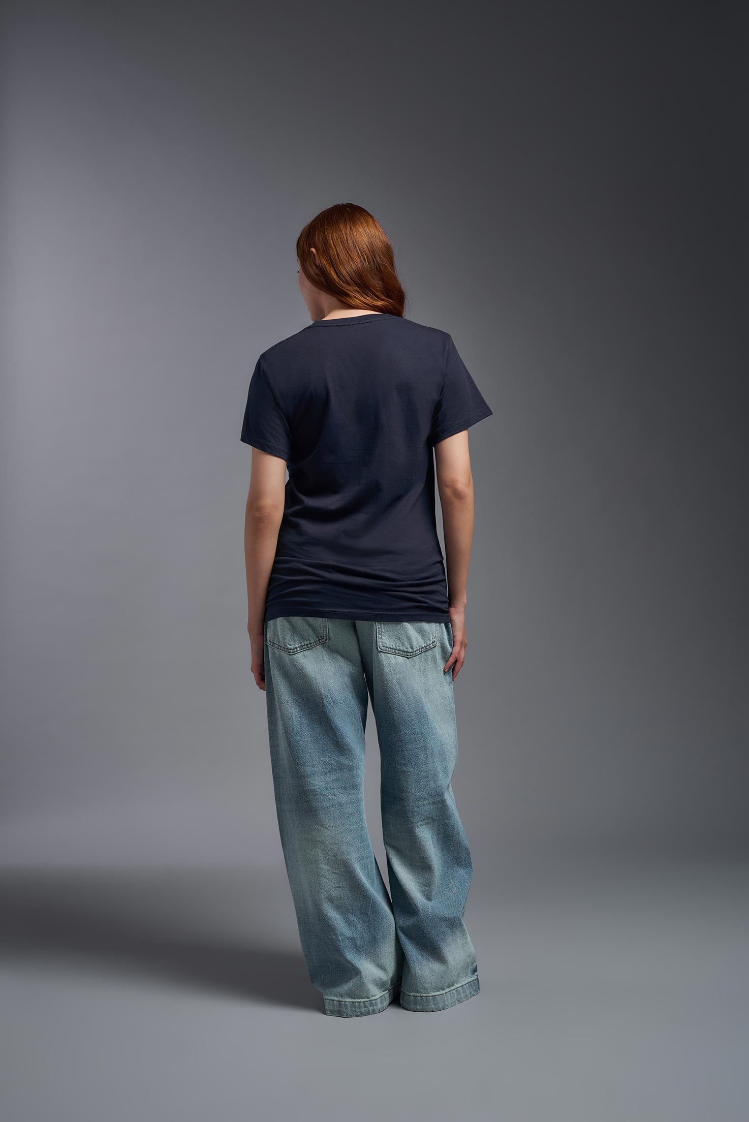A female model wearing the unisex Americana Cotton Soft Tee in the color navy, made from 100% combed ring-spun USA-grown cotton, showing the classic fit from a back view. This premium shirt is Made in the USA. #navy