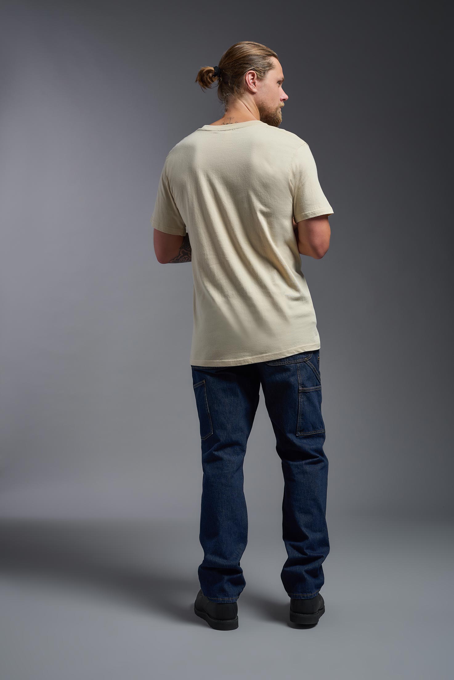 A male model wearing the unisex Americana Cotton Soft Tee in the color sand, made from 100% combed ring-spun USA-grown cotton, showing the classic fit from a back view. This premium shirt is Made in the USA. #sand