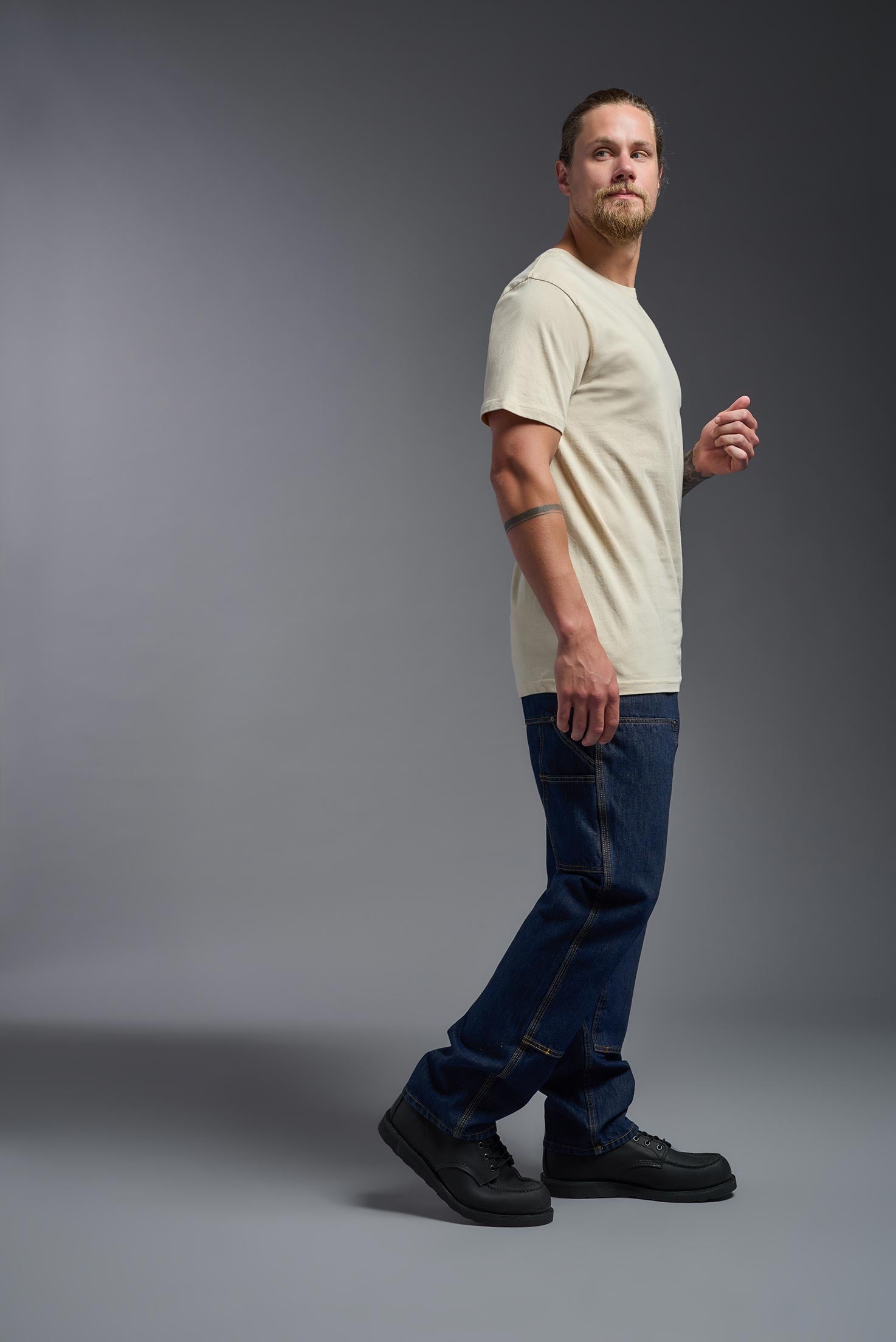 A male model wearing the unisex Americana Cotton Soft Tee in the color sand, made from 100% combed ring-spun USA-grown cotton, showing the classic fit from a side view. This premium shirt is Made in the USA. #sand