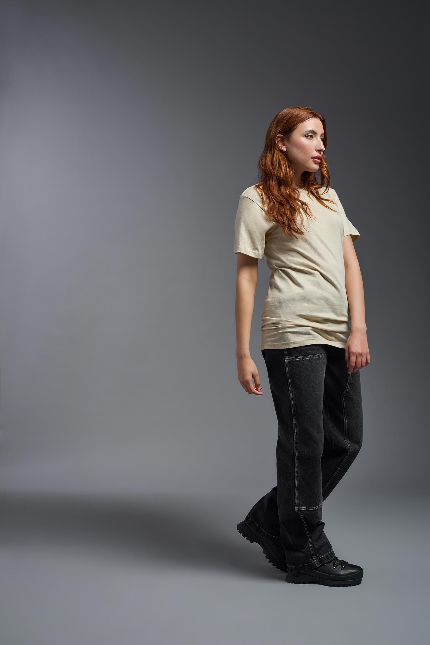 A female model wearing the unisex Americana Cotton Soft Tee in the color sand, made from 100% combed ring-spun USA-grown cotton, showing the classic fit from a side view. This premium shirt is Made in the USA. #sand
