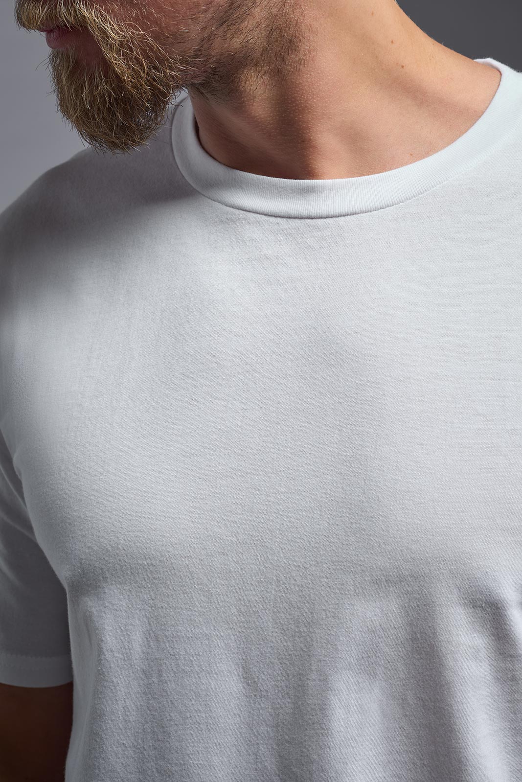 A male model wearing the unisex Americana Cotton Soft Tee in the color white, made from 100% combed ring-spun USA-grown cotton, showing the classic fit from a close-up collar view. This premium shirt is Made in the USA. #white