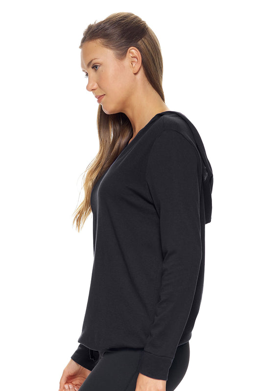 A female model with brown hair wearing the women's MoCA V-Neck Hoodie Shirt in the color black, made from a luxurious blend of 50% LENZING Modal and 50% Combed Ring-Spun Cotton, showing the relaxed fit from a side view. This fashion-forward, more sustainable t-shirt is elevated, eco-friendly, made in the USA, and available for bulk purchase. #black