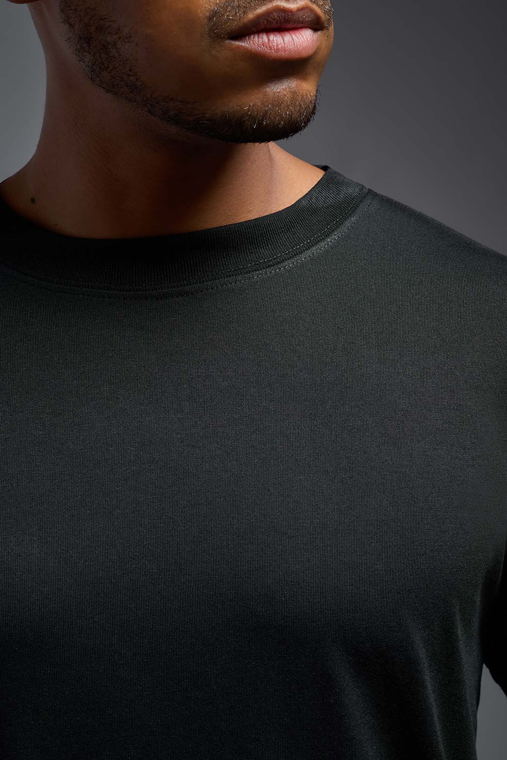 A male model wearing the men's DuroSoft Outdoor Tee in the color black, made out of 100% filament polyester, showing the modern fit from a collar close-up view. This shirt quick-dries and wicks moisture and is made in the USA. #black