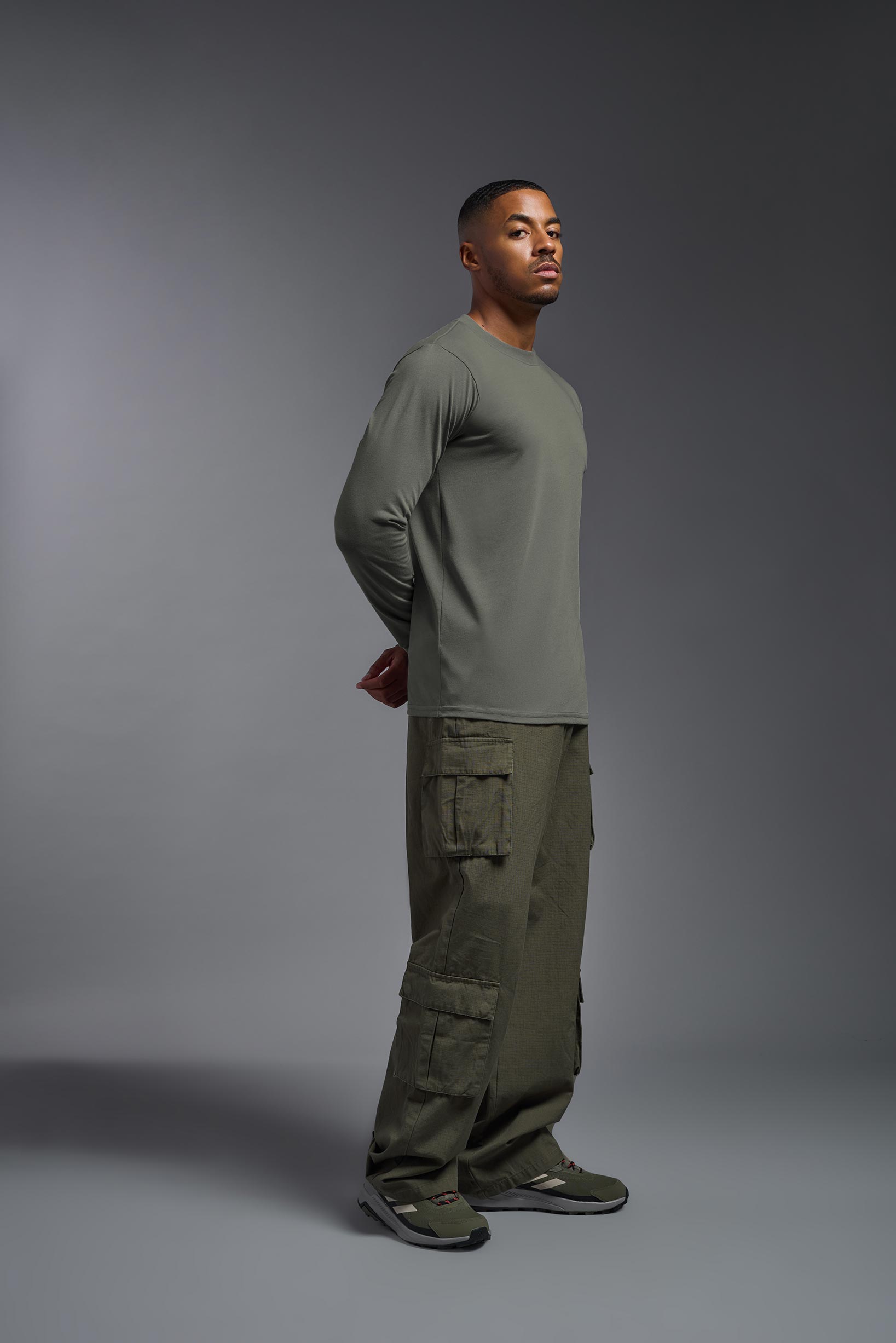 A male model wearing the men's DuroSoft Outdoor Long Sleeve in the color army gray made out of 100% filament polyester, showing the modern fit from a side view. This shirt quick-dries, wicks moisture and is made in the USA. #army-gray