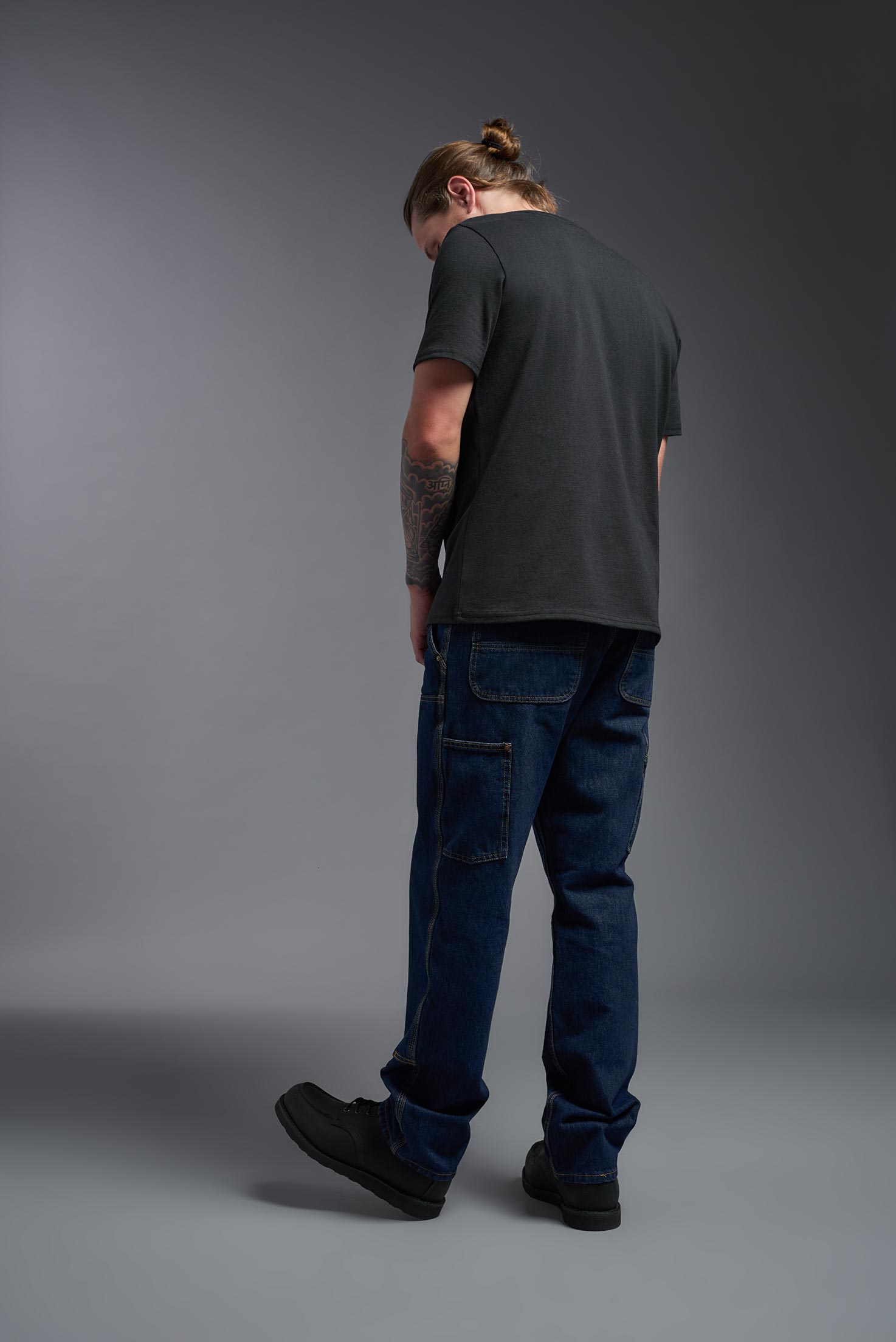 A male model wearing the unisex Imagen Short Sleeve Crewneck T-Shirt in the color black, made from 50% U.S. Grown Regenerative Cotton and 50% Recycled Polyester, showing the Relaxed Fit from a back view. This sustainable shirt is Made in the USA. #black