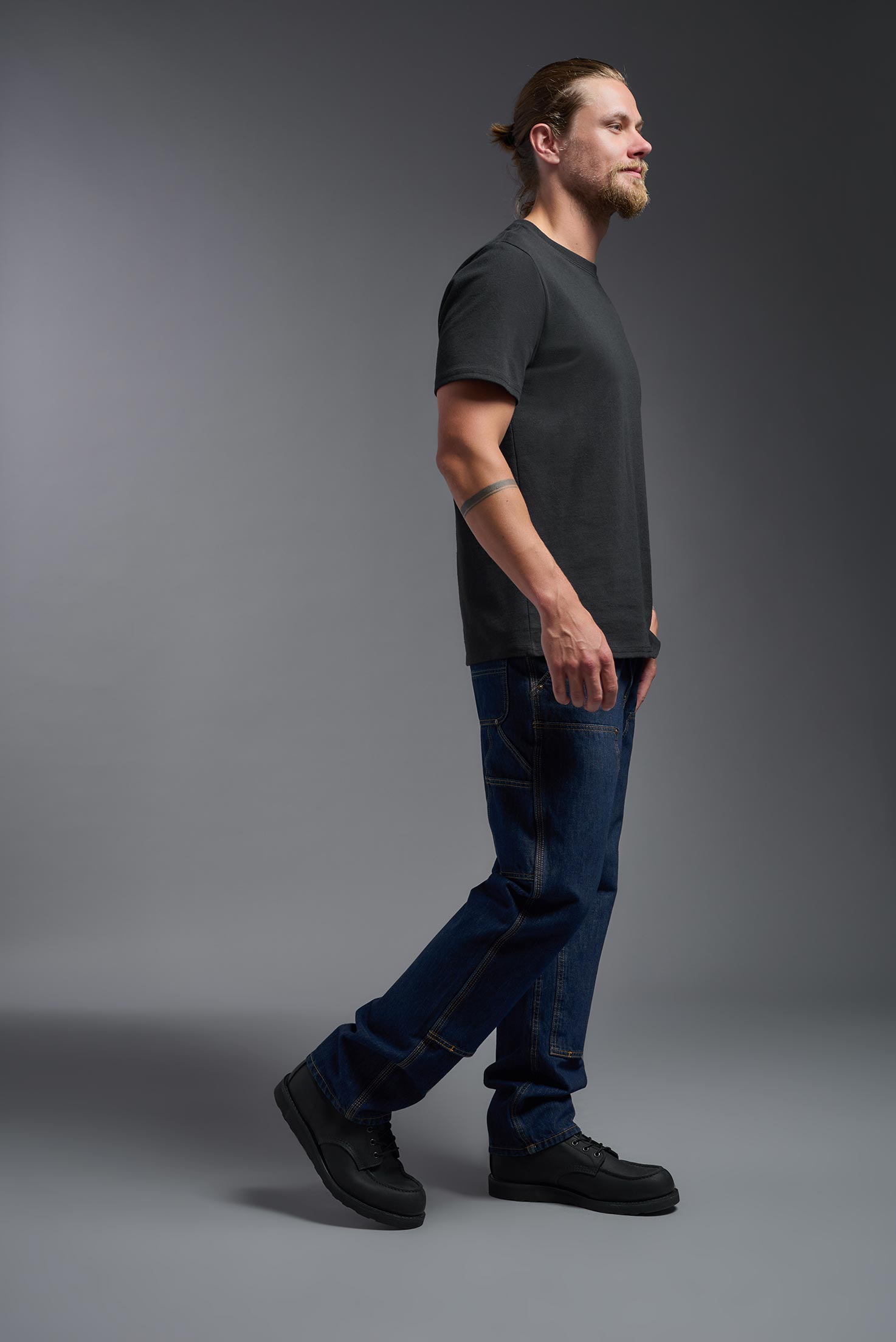 A male model wearing the unisex Imagen Short Sleeve Crewneck T-Shirt in the color black, made from 50% U.S. Grown Regenerative Cotton and 50% Recycled Polyester, showing the Relaxed Fit from a side view. This sustainable shirt is Made in the USA. #black