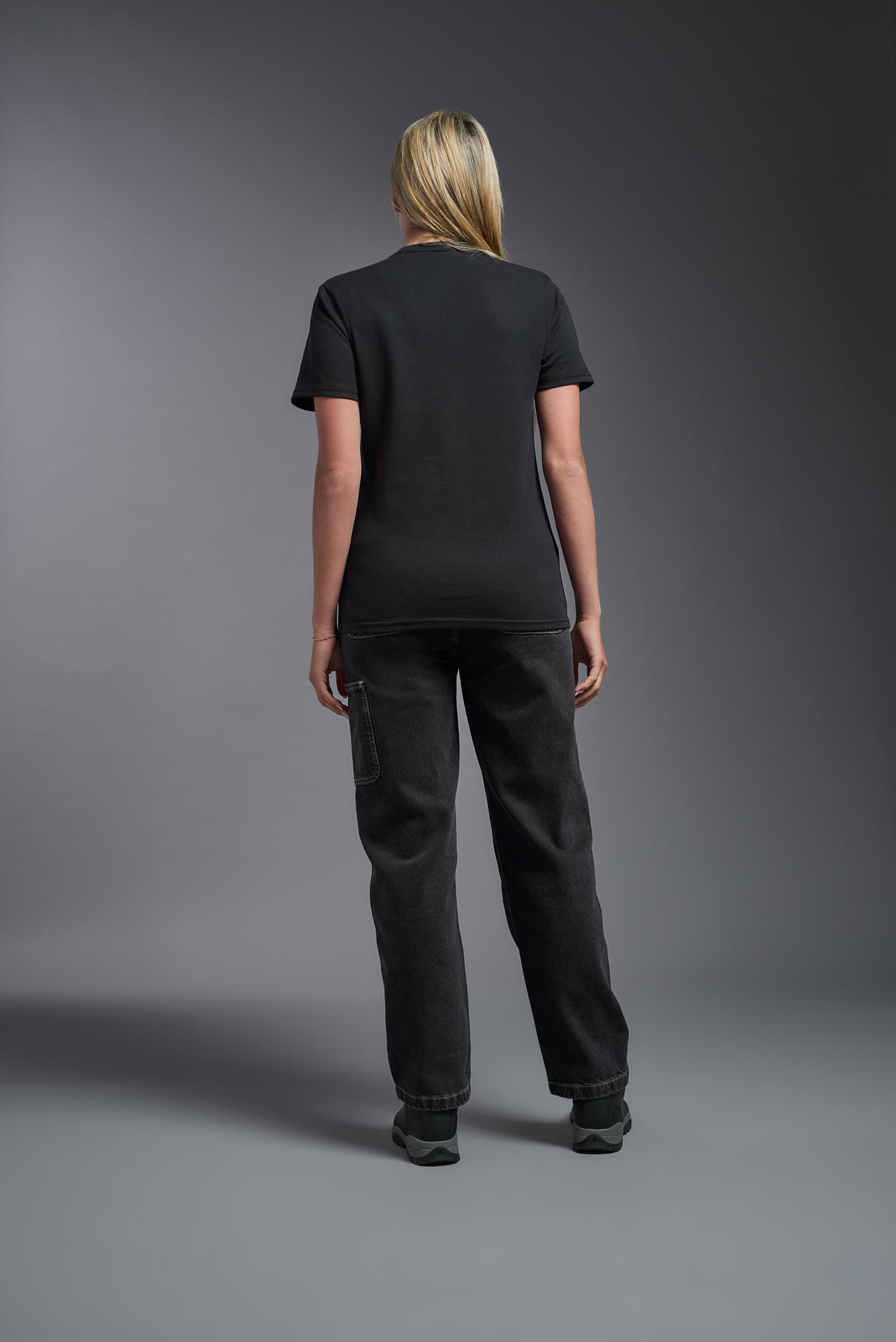 A female model wearing the unisex Imagen Short Sleeve Crewneck T-Shirt in the color black, made from 50% U.S. Grown Regenerative Cotton and 50% Recycled Polyester, showing the Relaxed Fit from a front view. This sustainable shirt is Made in the USA. #black