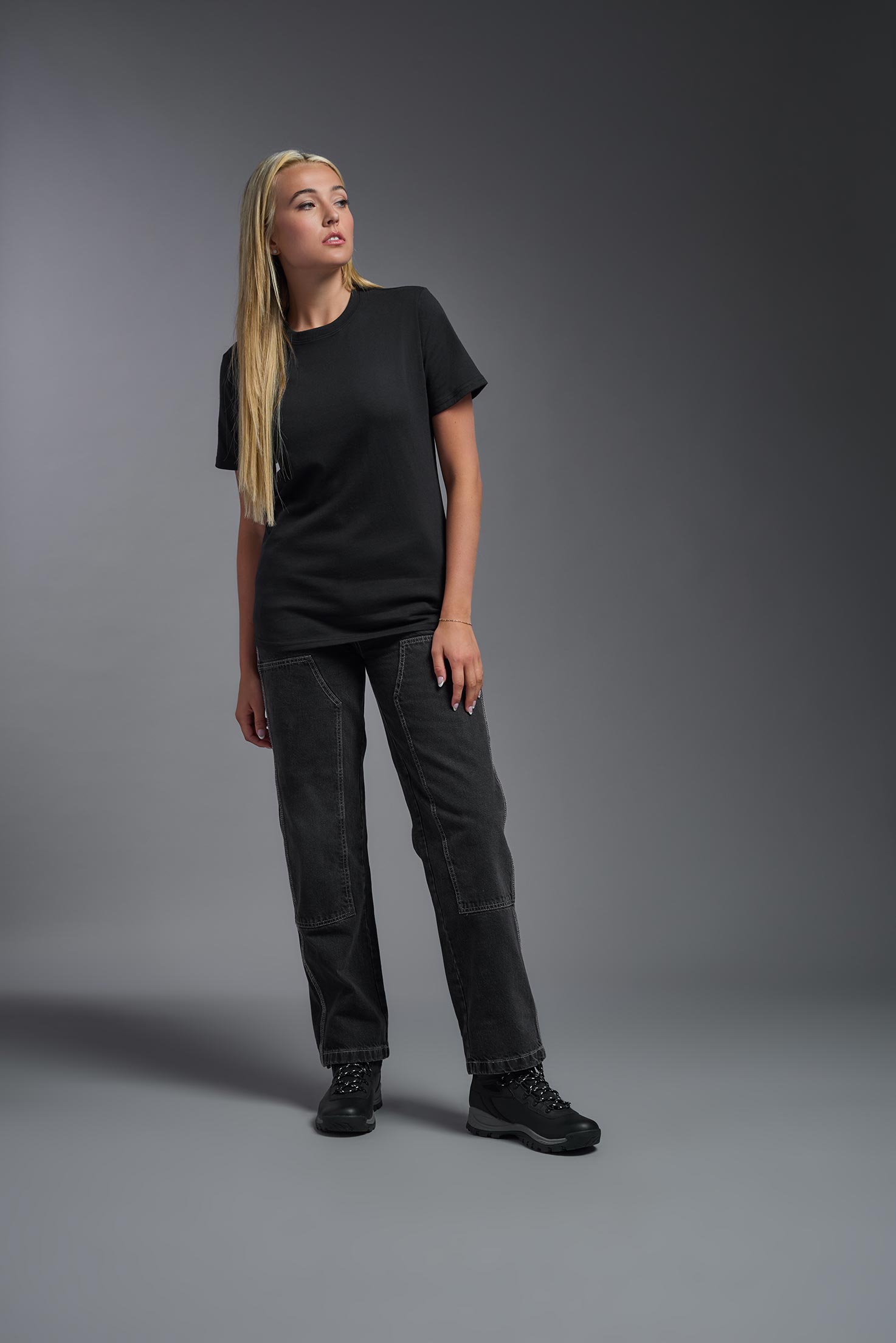 A female model wearing the unisex Imagen Short Sleeve Crewneck T-Shirt in the color black, made from 50% U.S. Grown Regenerative Cotton and 50% Recycled Polyester, showing the Relaxed Fit from a front view. This sustainable shirt is Made in the USA. #black