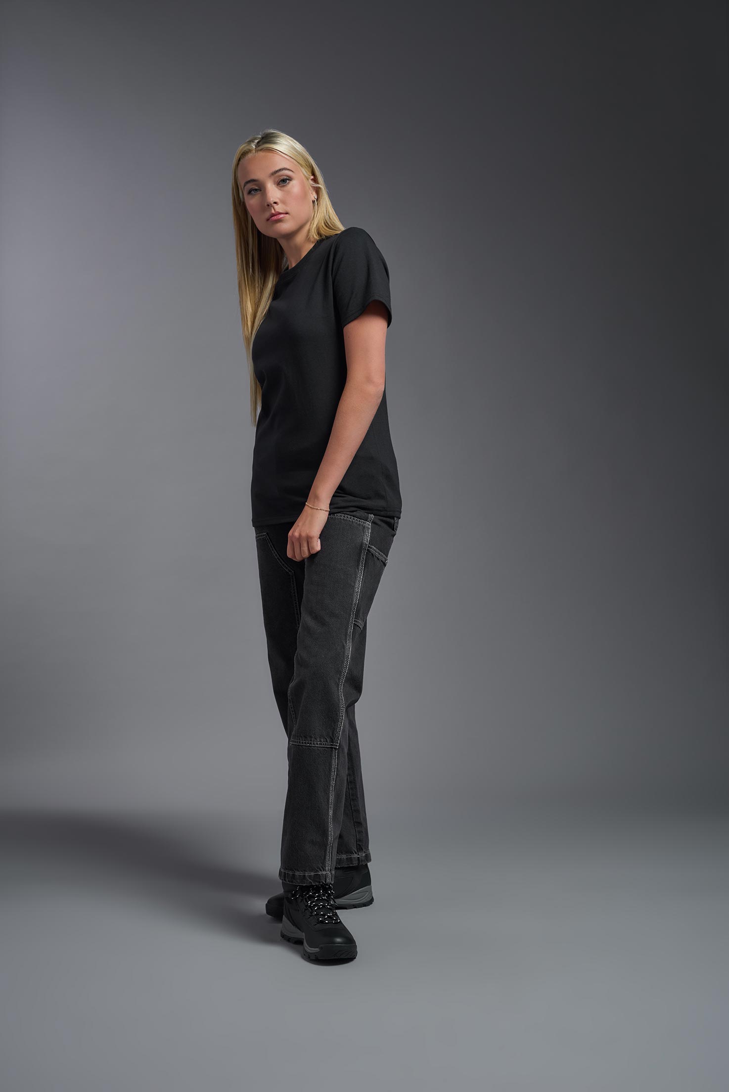 A female model wearing the unisex Imagen Short Sleeve Crewneck T-Shirt in the color black, made from 50% U.S. Grown Regenerative Cotton and 50% Recycled Polyester, showing the Relaxed Fit from a side view. This sustainable shirt is Made in the USA. #black
