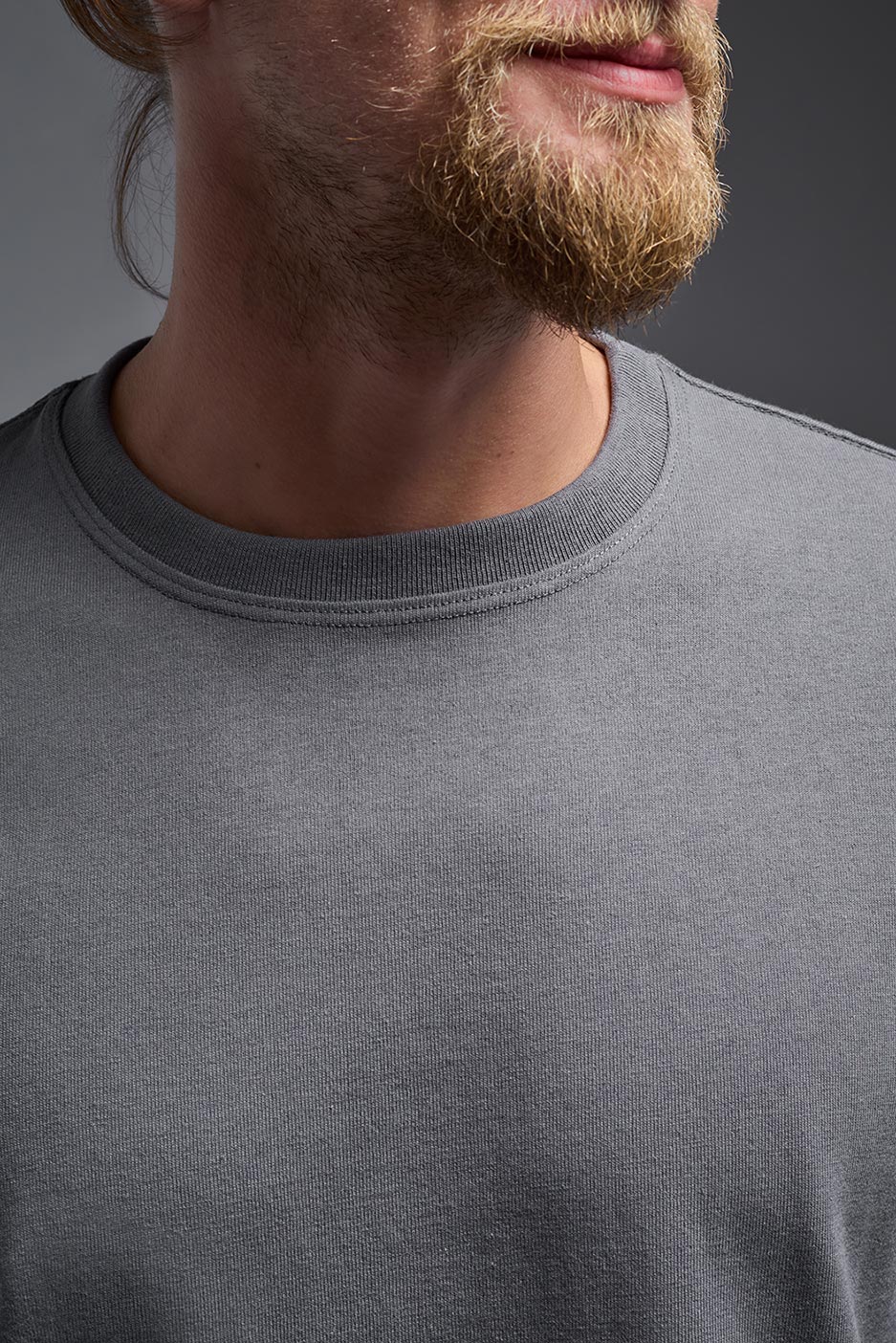 A male model wearing the unisex Imagen Short Sleeve Crewneck T-Shirt in the color carbon, made from 50% U.S. Grown Regenerative Cotton and 50% Recycled Polyester, showing the Relaxed Fit from a close-up collar view. This sustainable shirt is Made in the USA. #carbon