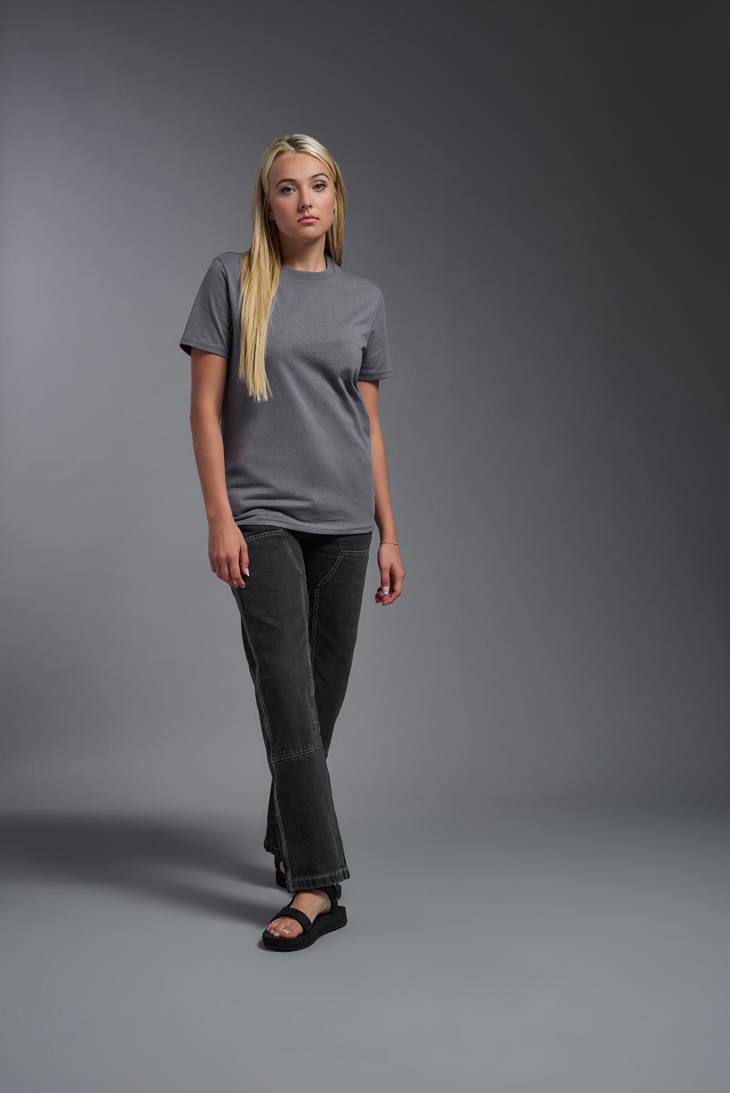 A female model wearing the unisex Imagen Short Sleeve Crewneck T-Shirt in the color carbon, made from 50% U.S. Grown Regenerative Cotton and 50% Recycled Polyester, showing the Relaxed Fit from a front view. This sustainable shirt is Made in the USA. #carbon