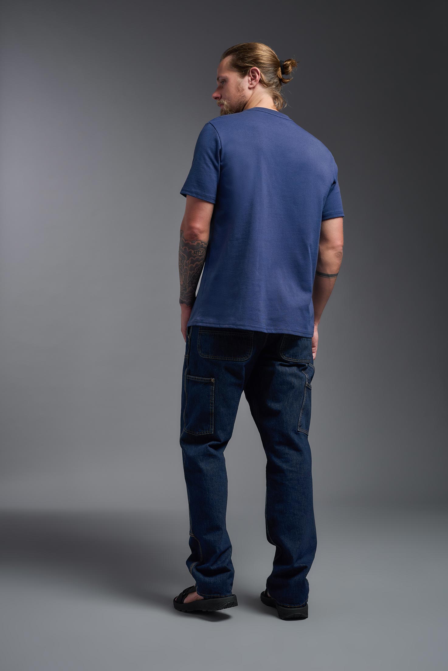 A male model wearing the unisex Imagen Short Sleeve Crewneck T-Shirt in the color navy, made from 50% U.S. Grown Regenerative Cotton and 50% Recycled Polyester, showing the Relaxed Fit from a back view. This sustainable shirt is Made in the USA. #navy