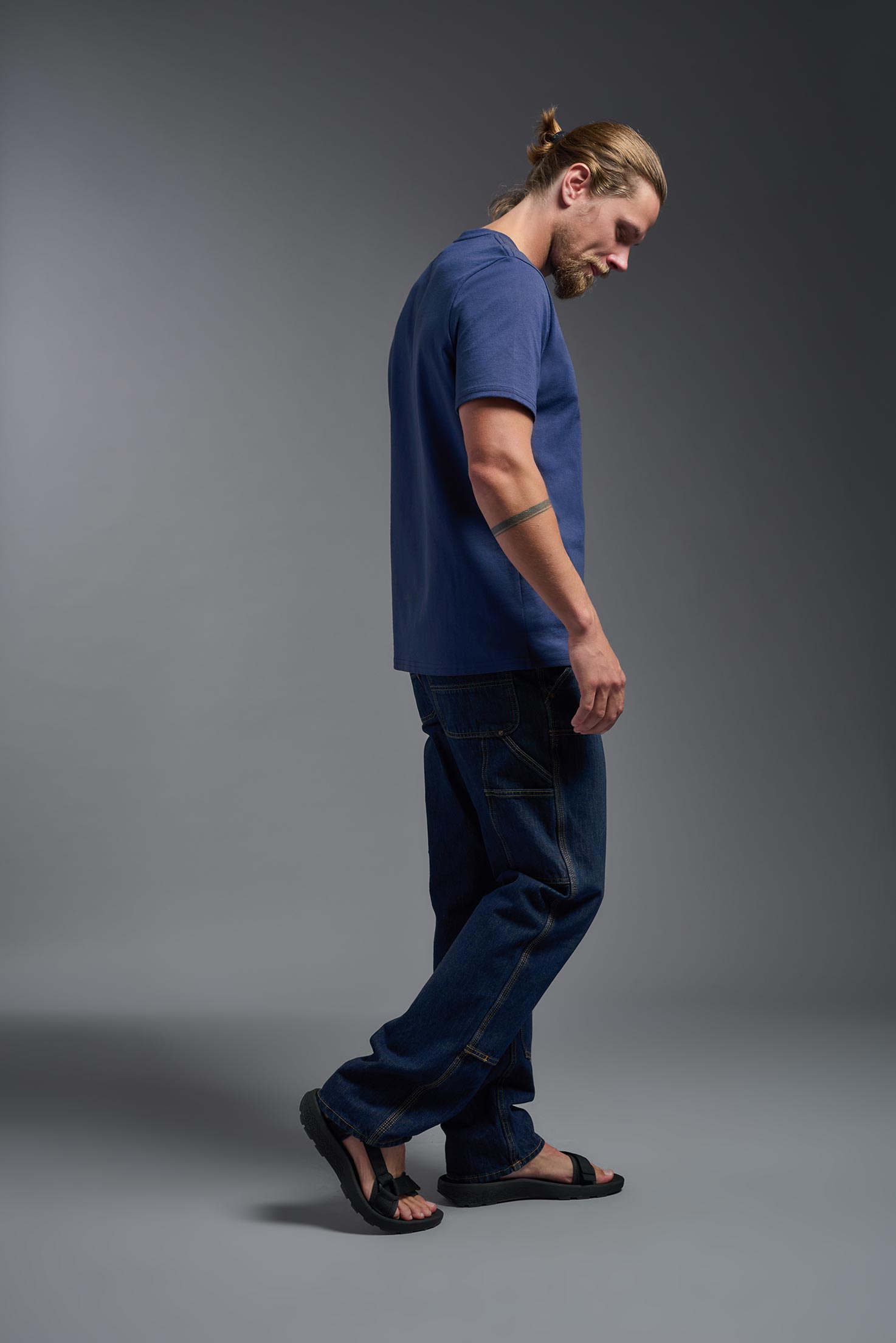 A male model wearing the unisex Imagen Short Sleeve Crewneck T-Shirt in the color navy, made from 50% U.S. Grown Regenerative Cotton and 50% Recycled Polyester, showing the Relaxed Fit from a side view. This sustainable shirt is Made in the USA. #navy