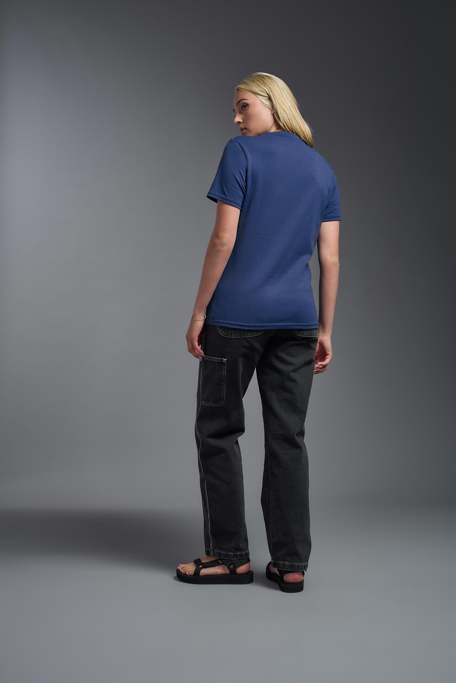 A female model wearing the unisex Imagen Short Sleeve Crewneck T-Shirt in the color navy, made from 50% U.S. Grown Regenerative Cotton and 50% Recycled Polyester, showing the Relaxed Fit from a back view. This sustainable shirt is Made in the USA. #navy