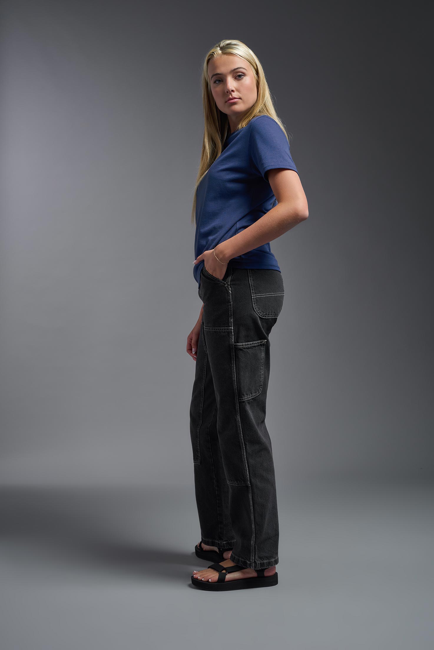 A female model wearing the unisex Imagen Short Sleeve Crewneck T-Shirt in the color navy, made from 50% U.S. Grown Regenerative Cotton and 50% Recycled Polyester, showing the Relaxed Fit from a side view. This sustainable shirt is Made in the USA. #navy